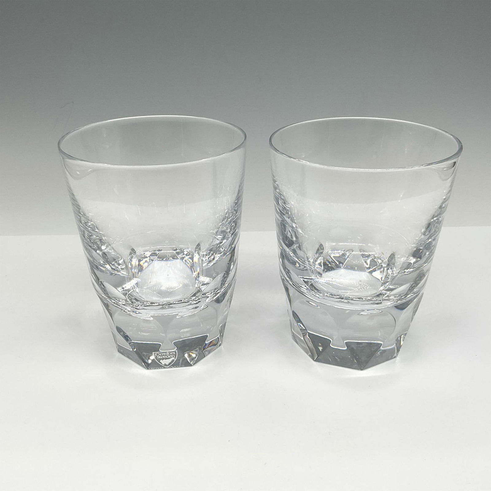 Orrefors Crystal Cocktail Glasses, Carat: Pair of clear crystal tumblers with triangle tapered base. Orrefors mark. This item has its original box: 9"L x 6"W x 6"H. Issued: 21st century Dimensions: 4.5"H x 3.25" dia. Manufacturer: Orrefors Co