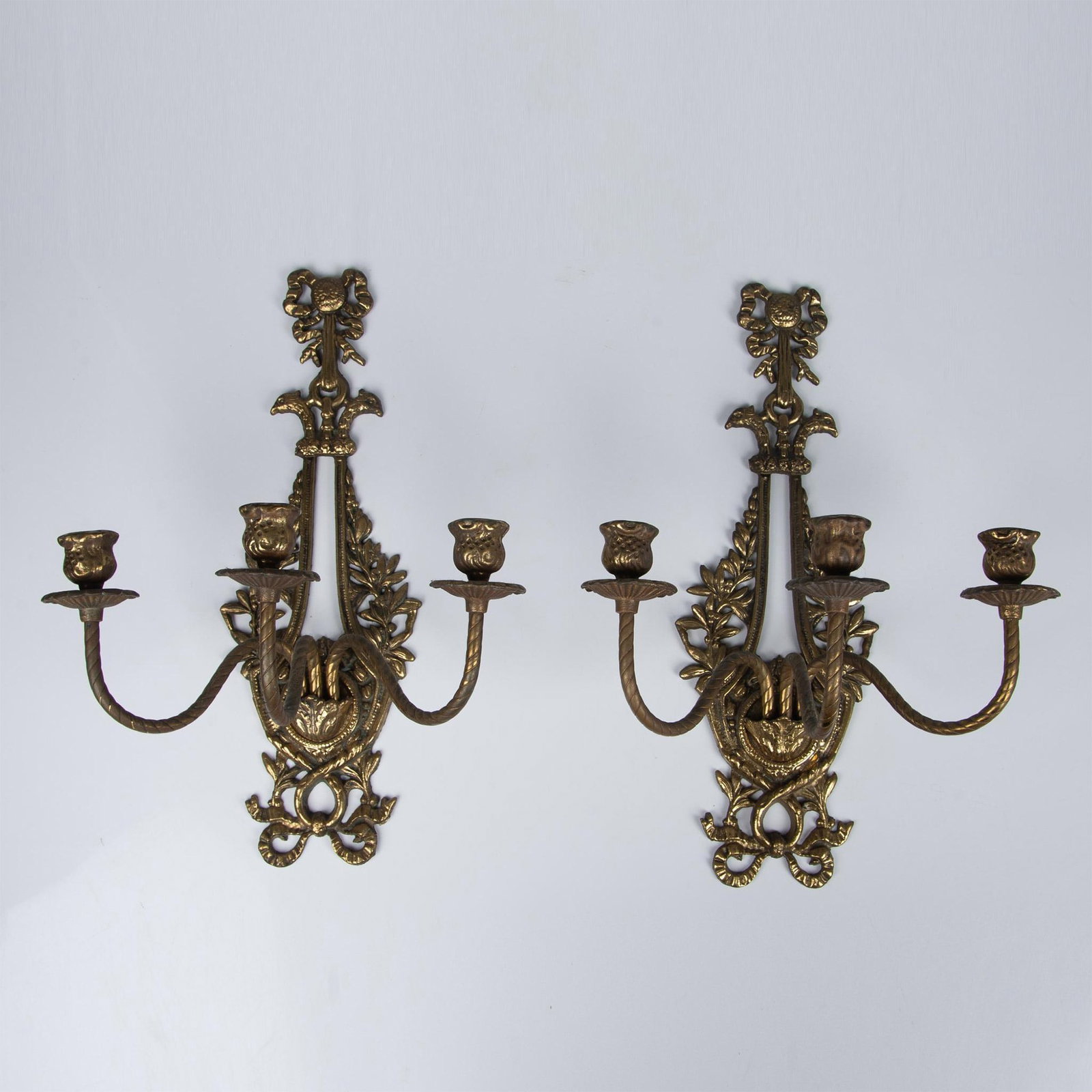 Pair of French Louis XV Style Bronze Three-Armed Sconces: Exquisite decorative wall candle sconces boasting floral and leaf tiered scrolling arms in Rococo style gilded bronze. Adorned with stunning bow and peacock details, these sconces exude ornate, high-q