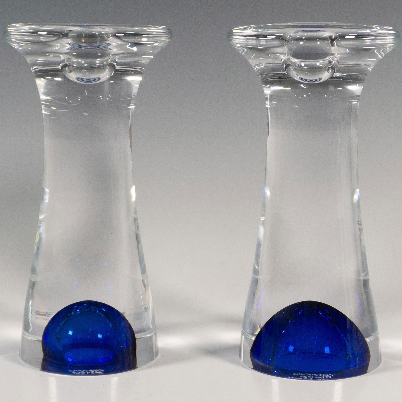 Pair of Kosta Boda by Goran Warff Candlestick Holders, Zoom: A set of two clear glass abstract form candle holders accented with blue glass bubble at the bottom. Kosta Boda etched on the undersides. Artist: Goran Warff Dimensions: 3.25"W x 6.75"H Manufacturer: