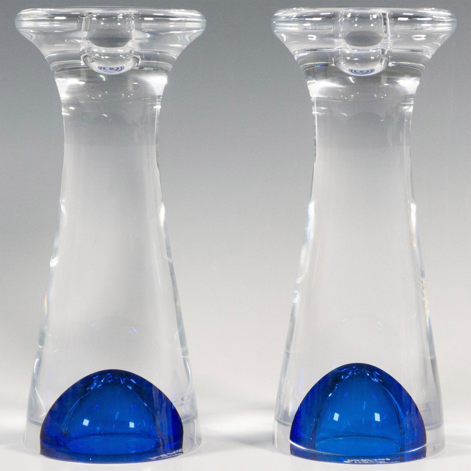 Pair of Kosta Boda by Goran Warff Candlestick Holders, Zoom: A set of two clear glass abstract form candle holders accented with blue glass bubble at the bottom. Kosta Boda etched on the undersides. Artist: Goran Warff Dimensions: 3.5"W x 8"H Manufacturer: Kost