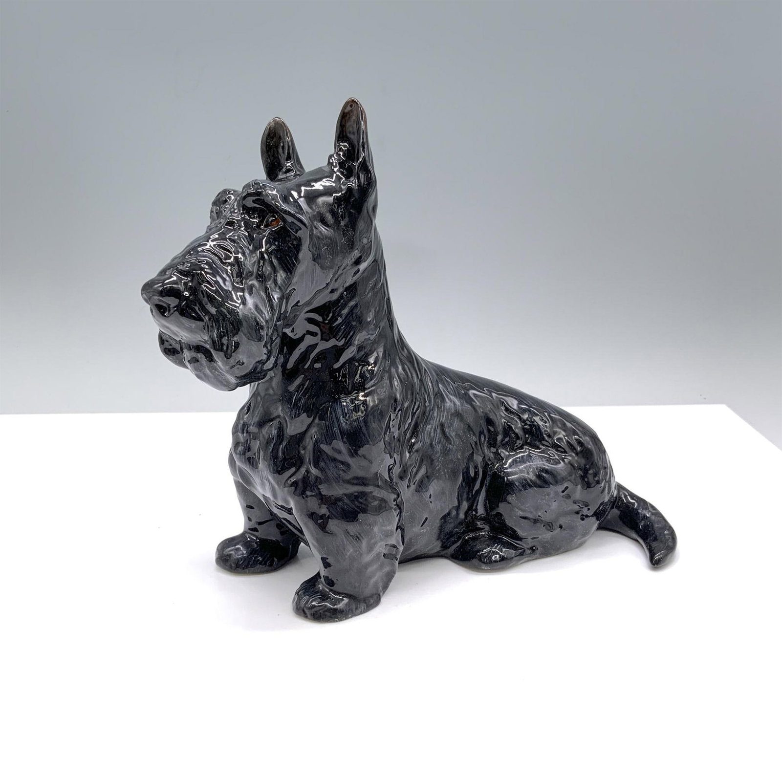 Seated Scottish Terrier - HN1017 - Royal Doulton Animal Figurine: Model number 733. This is the largest of the seated Scotty figurines. It is bone China with glossy black fur. Royal Doulton backstamp is on the bottom. Issued: 1931-1946 Dimensions: 9"L x 3.5"W x 7"H 