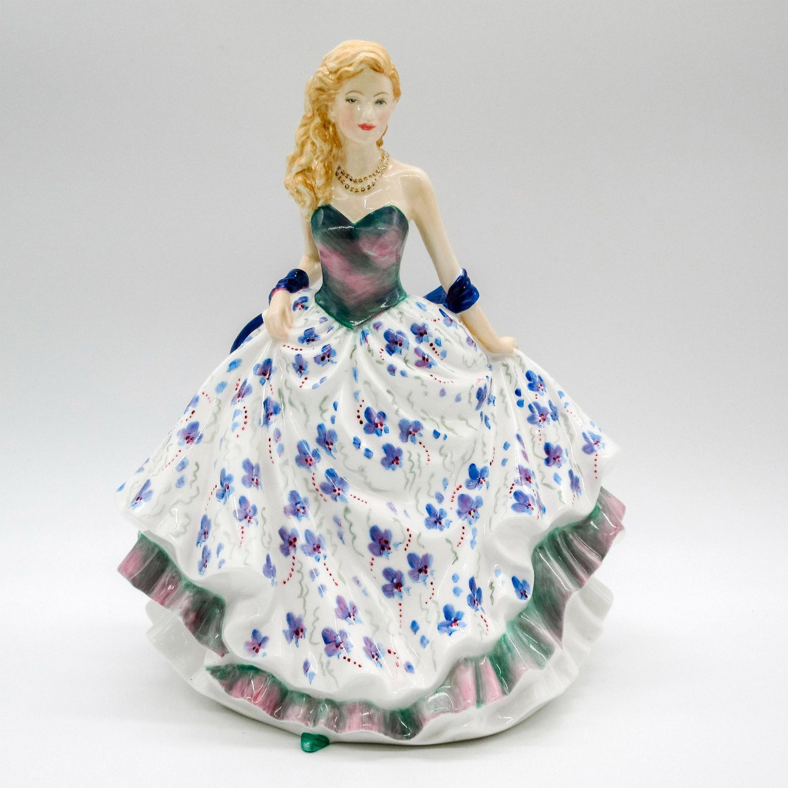 Lovely Lady, Gilded Prototype - Royal Doulton Figurine: Bone china; blonde beauty in a ruffled gown. Green and pink bodice, white skirt with violet flowers, and gilded necklace Royal Doulton Prototype Only backstamp. Dimensions: 5.75" L x 7.25" W x 8.5" H 