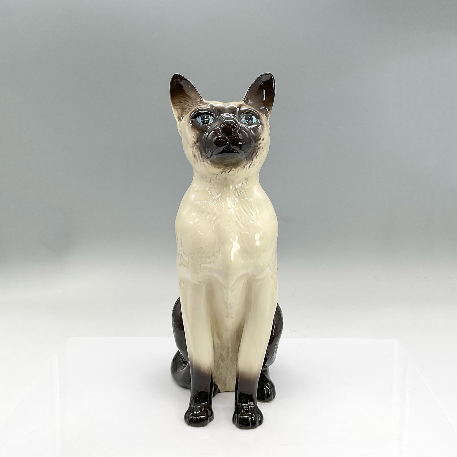 Royal Doulton Figurine, Siamese Cat Seated DA83: Cream and black bone china figure of a seated Siamese cat with blue eyes. Royal Doulton backstamp. Issued: 20th century Dimensions: 6"L x 5"W x 13.75"H Manufacturer: Royal Doulton Country of Origin: E