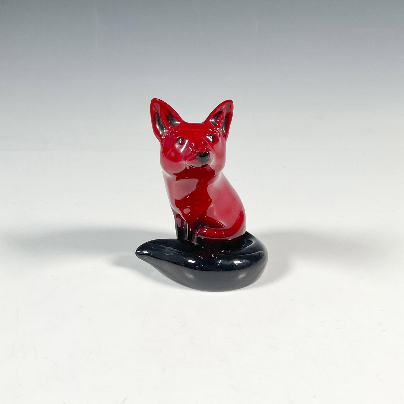 Royal Doulton Flambe Figurine, Fox Seated HN147B: In the deep rich red glaze, seated Fox with curled tail. Gloss finish. Royal Doulton backstamp in black. Issued: 20th century Dimensions: 3.75"L x 3.25"W x 4.25"H Manufacturer: Royal Doulton Country o