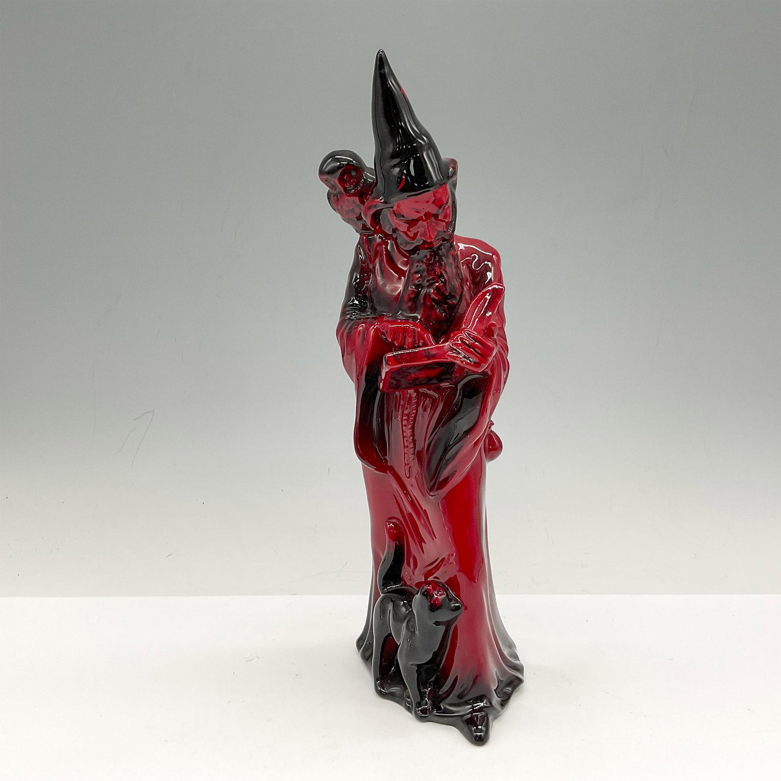 The Wizard HN3121 Flambe - Royal Doulton Figurine: Red flambe glossy figural reading a spell from his book with his black cat at his feet looking up at him. Royal Doulton backstamp. Artist: A. Maslankowski Issued: 1990 - 1995 Dimensions: 3.25"L x 3.25