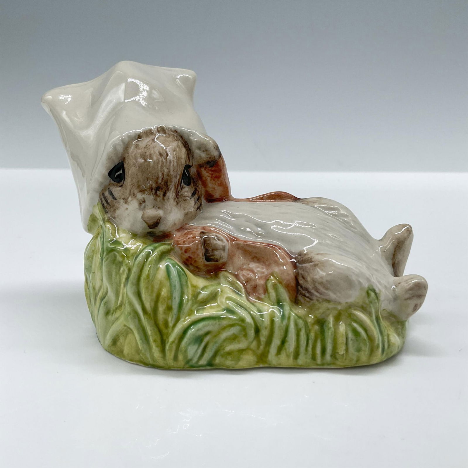 Royal Albert Beatrix Potter Figurine, Benjamin Bunny Wakes Up: Glossy porcelain, features Benjamin Bunny character lying on a green grassy base. Royal Albert backstamp. Issued: c. 1990 Dimensions: 2''L x 3''W x 3''H Manufacturer: Royal Albert Country of Origin: E