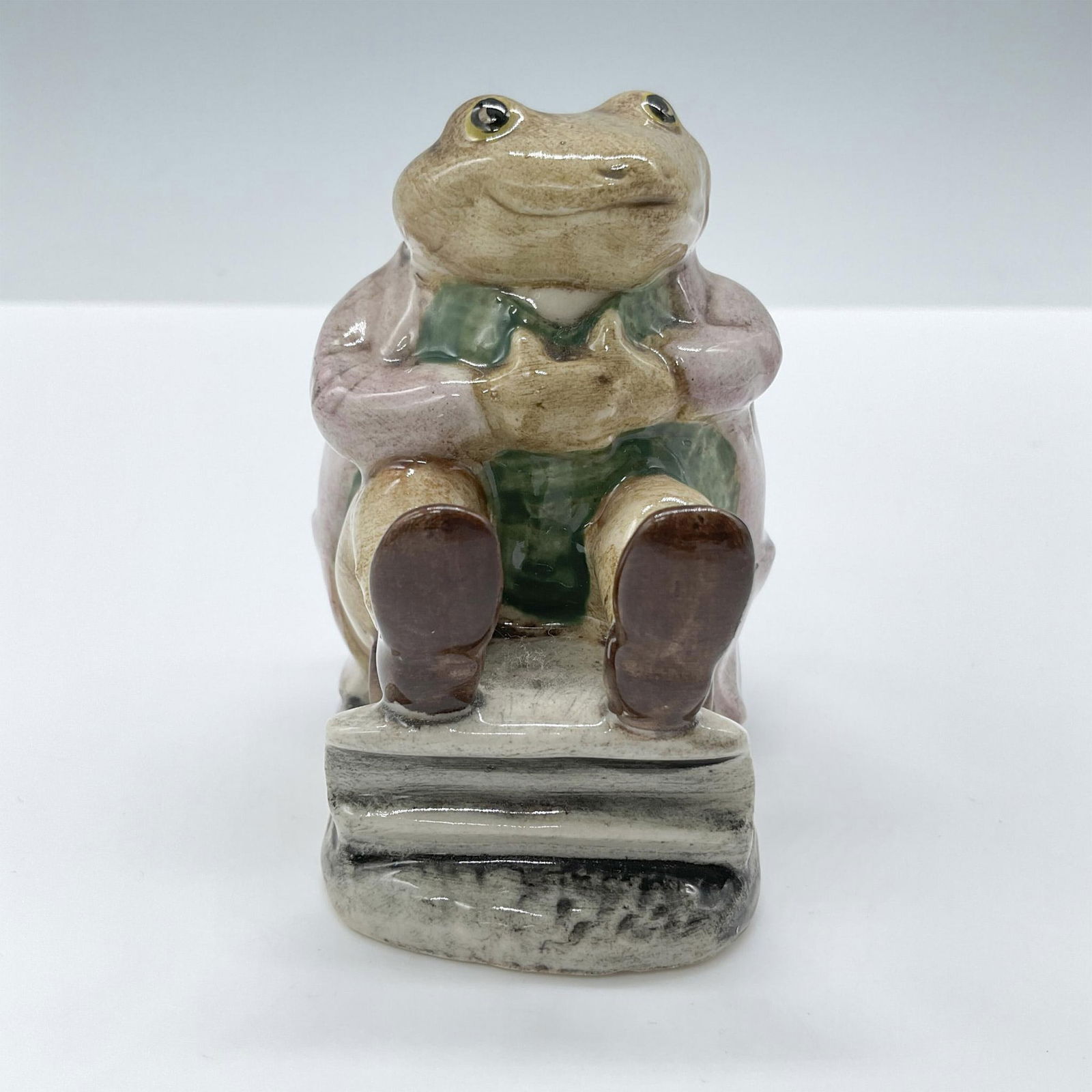 Royal Albert Beatrix Potter Figurine, Mr Jackson: Glossy porcelain, depicts the frog character wearing a mauve jacket sitting on a rocking chair. Royal Albert backstamp. Artist: Albert Hallam Issued: c. 1989 Dimensions: 2.75''L x 1.75''W x 3''H Manuf