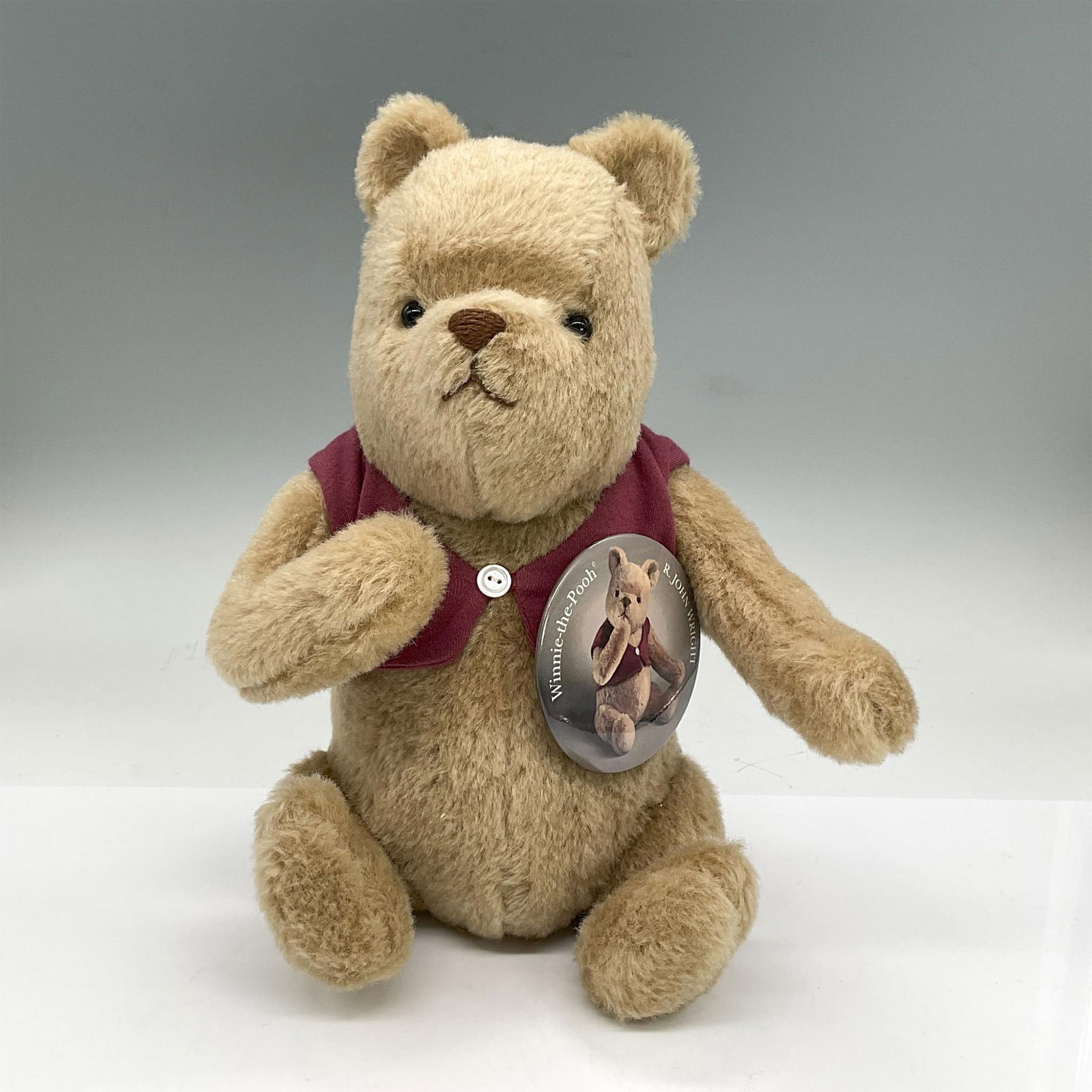 R. John Wright Stuffed Animal, Classic Winnie The Pooh: Tan early version of Winnie seated in a short red vest seat. Moveable head, arms and legs. Includes Certificate of Authenticity Dimensions: 8"L x 4"W x 12.25"H Edition Number: 1171 of 2500 Manufacture