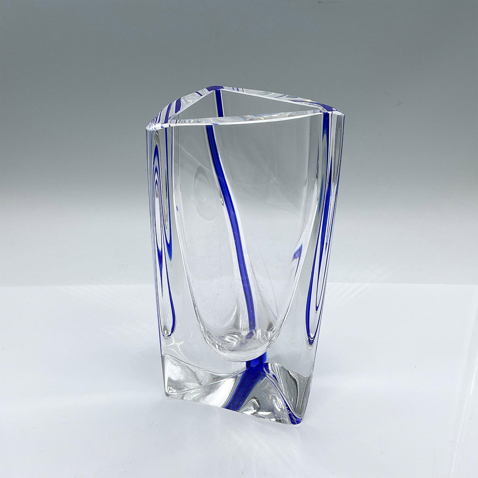 Kosta Boda by Goran Warff Glass Triangular Vase: Clear triangular form flower vase with a slight twist, adorned with a cobalt-blue glass vertical band. Artist etched signature. Kosta Boda marked on the underside. Artist: Goran Warff Issued: Late 20t