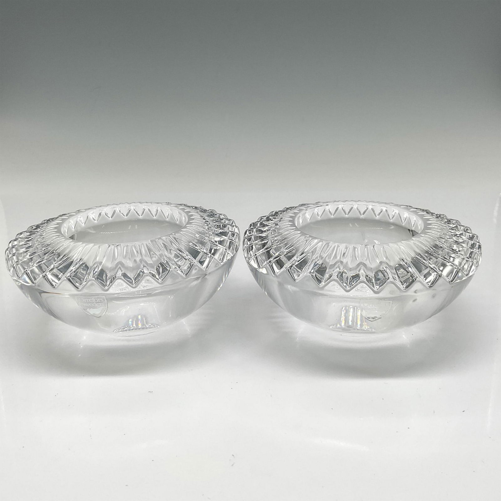 Pair of Orrefors Crystal Brilliance Votives: Round clear crystal base rimmed with pleat cut crystal. Orrefors mark. 6719483. This item has its original box: 5"L x 5"W x 2.25"H. Issued: 21st century Dimensions: 2.25"H x 4.25" dia. Manufacturer: O