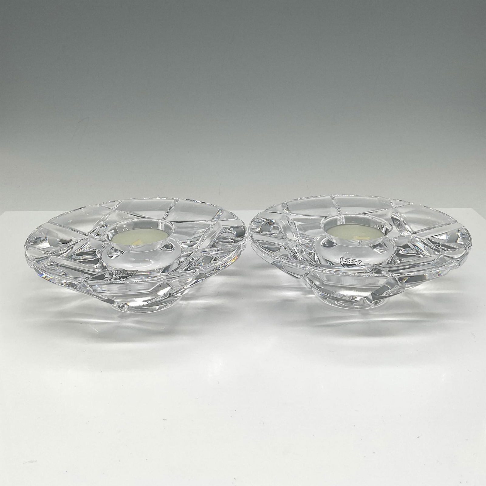 Pair of Orrefors Crystal Madison Votives: Cut crystal in checkerboard pattern on reverse with clear smooth crystal top and center holder for tealight. Orrefors mark. This item has its original box: 6.25"L x 6"W x 2.50"H. Artist: Marti Rytkone