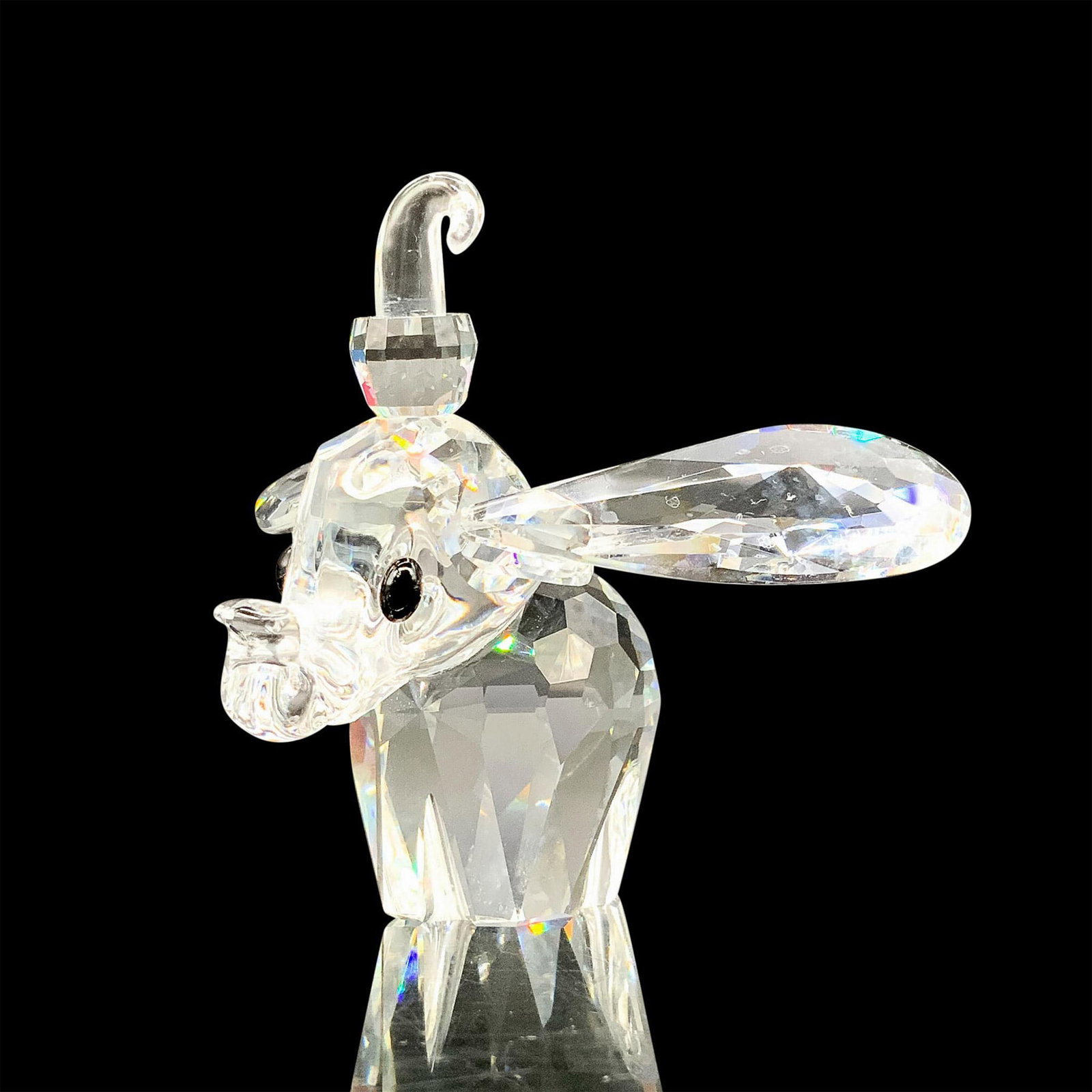 Swarovski Crystal Figurine, Dumbo 7640NR100: A clear crystal figure of Dumbo with his ears and trunk raised a bit. Black crystals are used for the eyes. Swarovski backstamp. This item has its original box. Dimensions of the original box: 6"H x 5