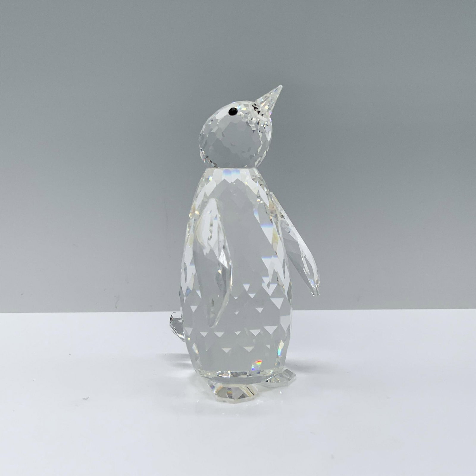 Swarovski Crystal Figurine, Penguin 010008: A clear penguin stands proudly with its wings slightly opened and its head tilted upwards in wonder. Swarovski backstamp. This item has its original box. Dimensions of the box: 6"H x 5" dia. Artist: M