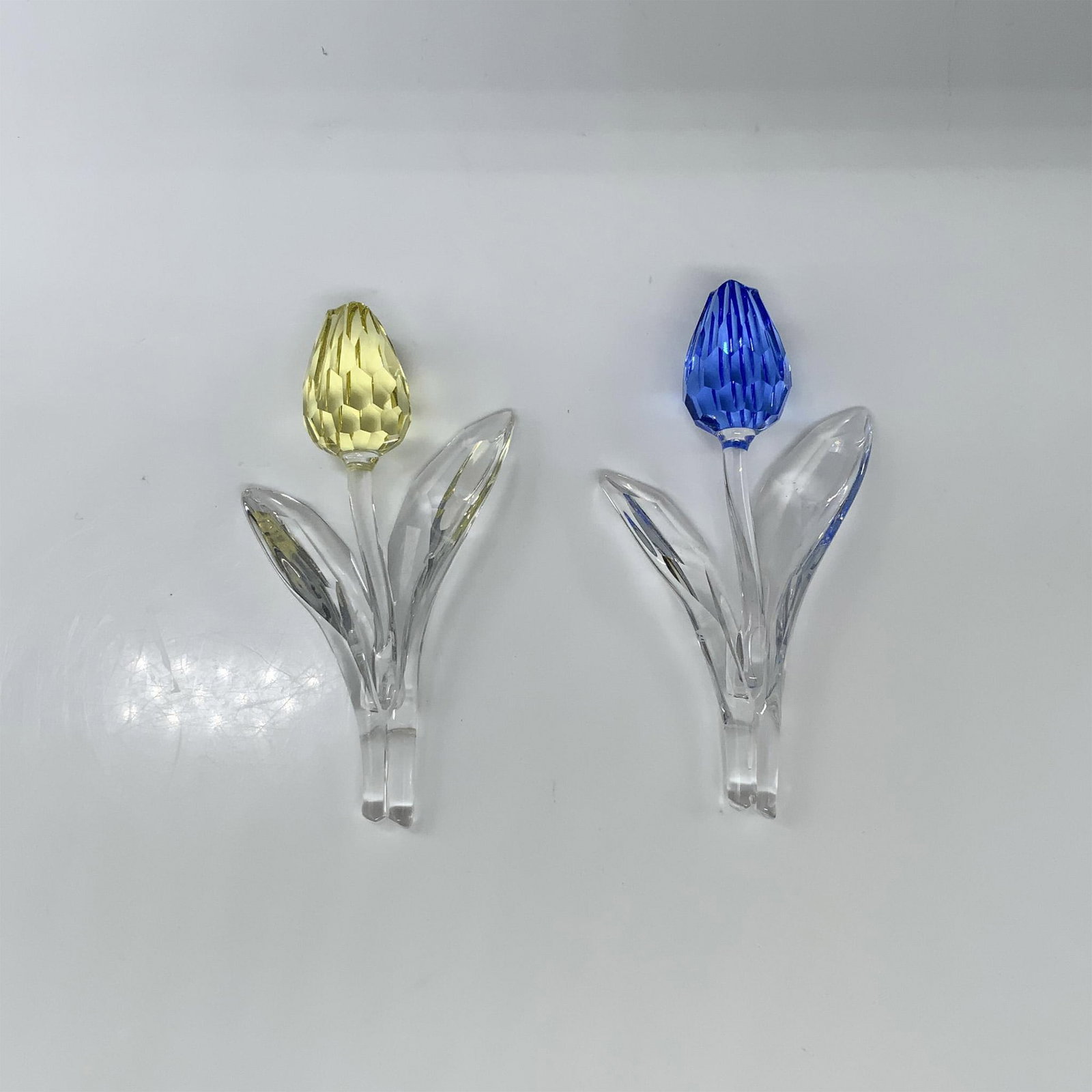 2pc Swarovski Crystal Figurines, Blue and Yellow Tulip: Explore our delightful set featuring two tulips with a blue bulb (606546) and a yellow bulb (657335), each adorned with two vibrant leaves and exquisitely crafted stems. This item has its original box