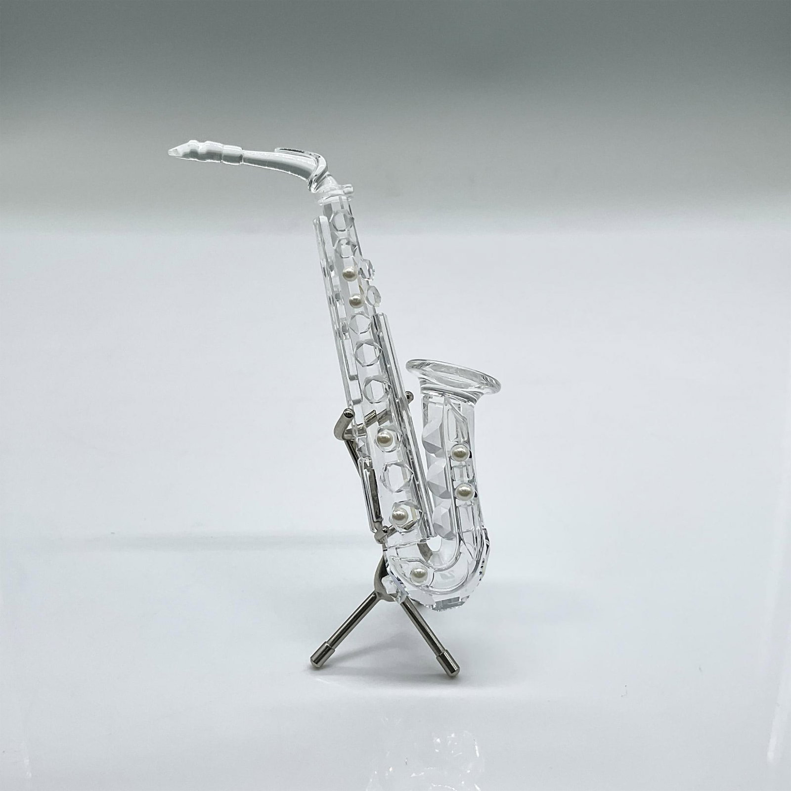 Swarovski Silver Crystal Figurine, Saxophone on Stand: Sparkling clear saxophone with pearlized accents. Swarovski etched mark. Includes original box: 6"H x 3.25"dia. Issued: 1997-2003 Dimensions: 1.5"L x 2.75"W x 4"H Manufacturer: Swarovski Country of Or