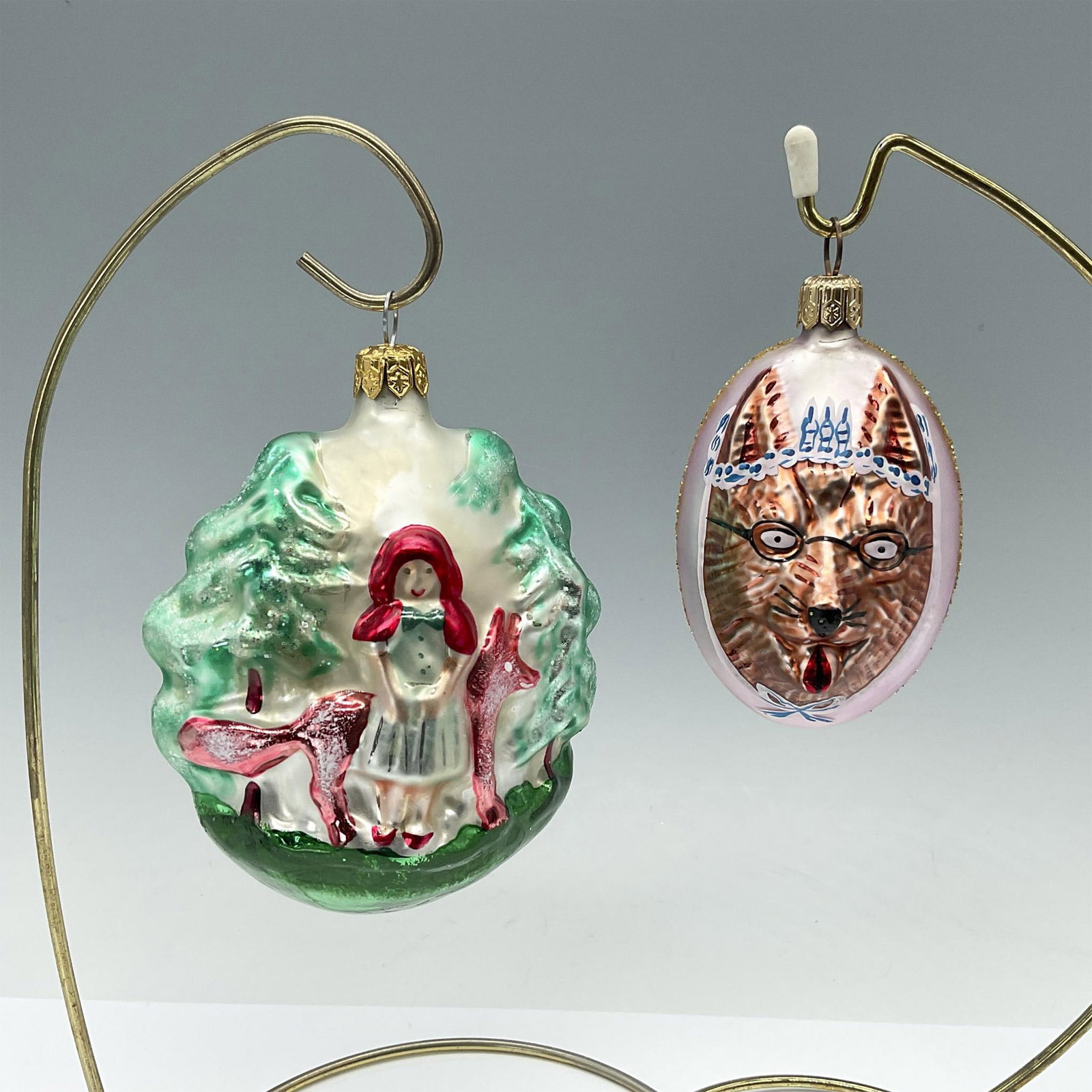2pcr Radko Style Christmas Ornaments, Little Red Riding Hood: Two charming ornaments depicting scenes from the Little Red Riding Hood nursery rhyme. One showcases Red and the Wolf, while the other depicts the cunning wolf with two faces. Larger piece measures 3.