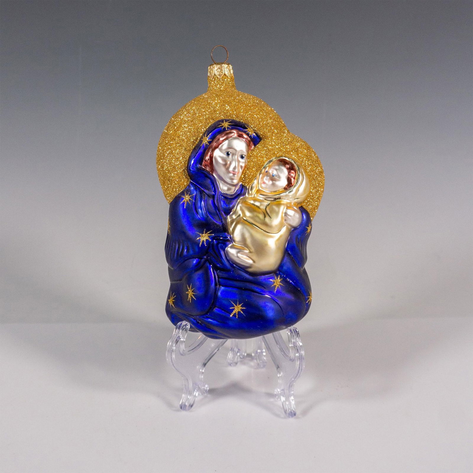 Patricia Breen Christmas Ornament, Madonna of the Night Blue: Exquisitely mouth-blown and hand-painted, this glass ornament portrays the Madonna with child in a stunning deep blue hue, enriched with radiant gold accents and adorned with sparkling gold glitter. I