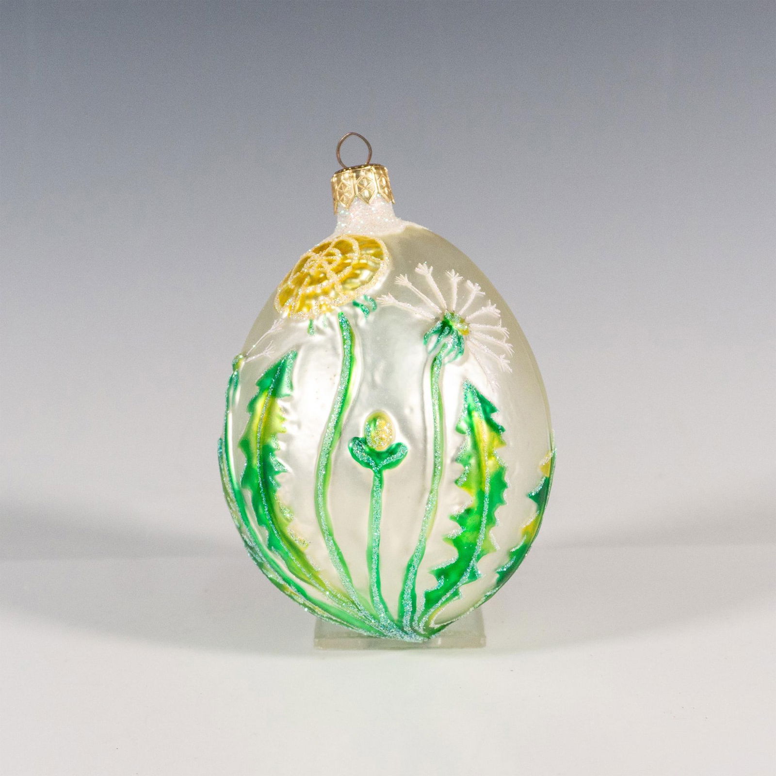 Patricia Breen Christmas Ornament, Dandelion Egg: Exquisitely hand-painted, this egg-shaped glass ornament features a matte white base adorned with delicate green dandelion leaves gracefully growing up the sides of the bulb. Inspired by the book Dand