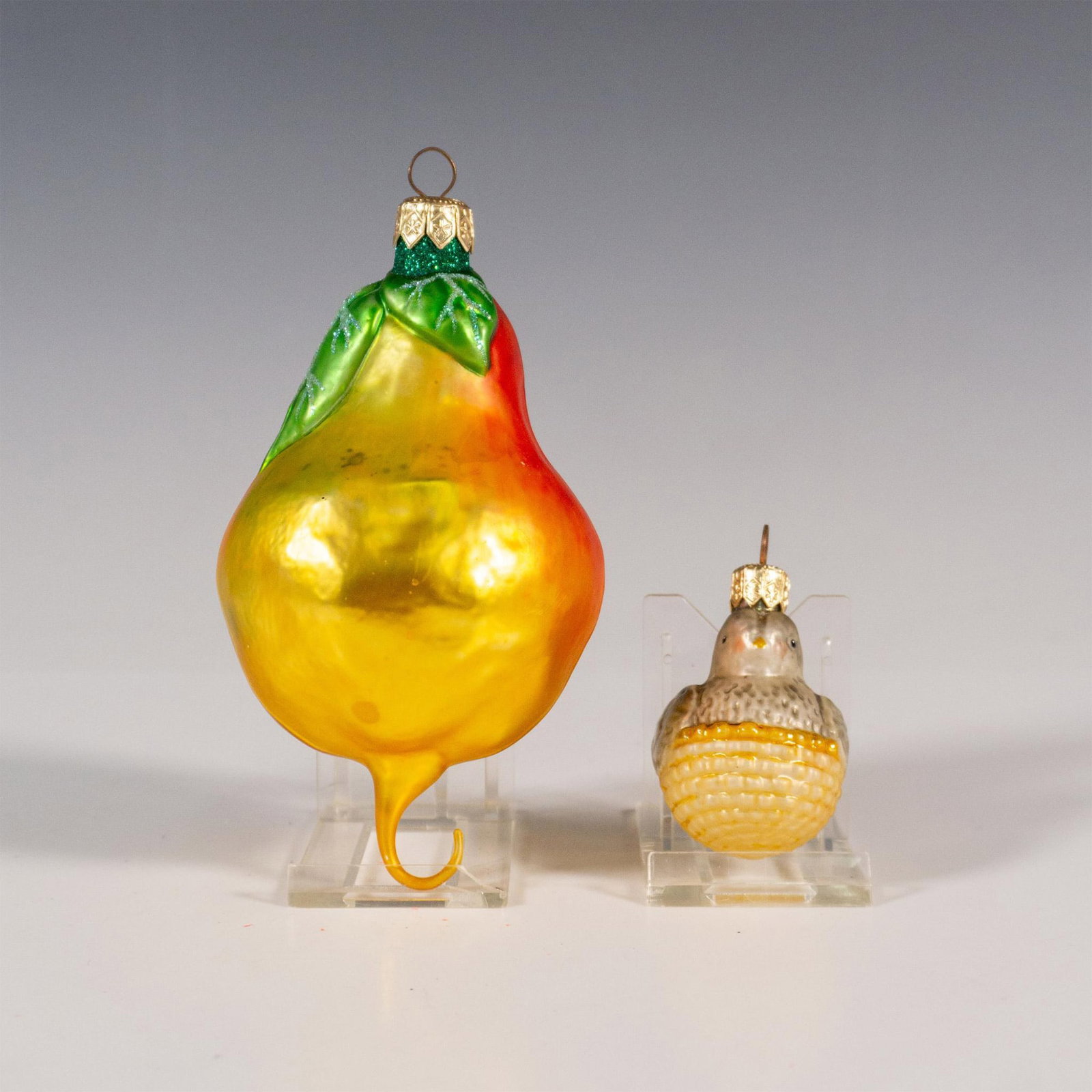 2pc Patricia Breen Ornaments, Partridge in a Pear Tree: This charming pair consists of a radiant handcrafted pear ornament with a hook on the base, perfect for carrying a small bird in a basket. The design depicts a partridge in a pear tree, inspired by th