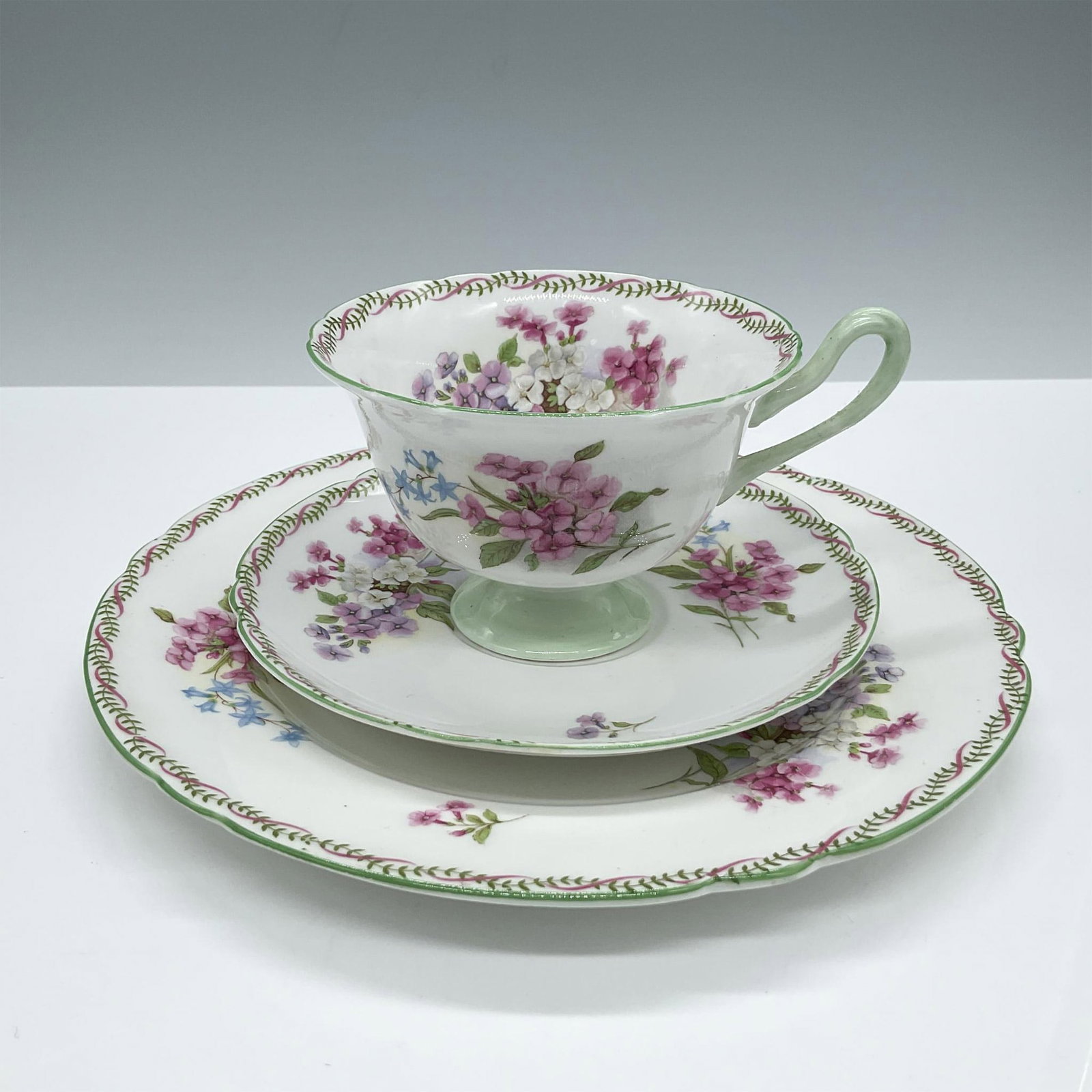 Shelley Bone China Tea Trio, Floral: This beautiful set features a delicate floral design enhanced with green and pink details. Includes tea cup, saucer and plate. Shelley backstamp. Issued: 20th century Dimensions: Cup: 4''L x 5''W x 2.