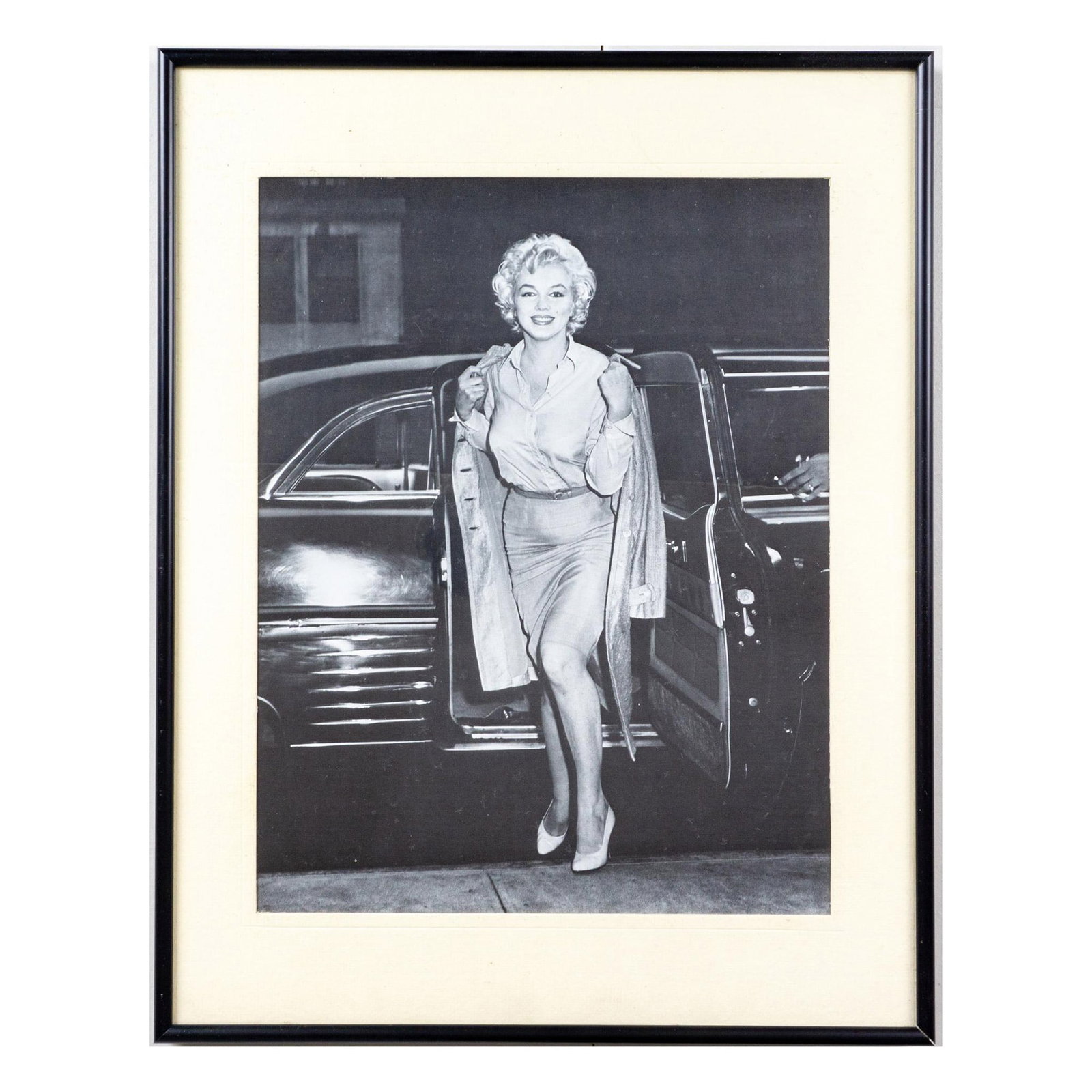 Paparazzi Style Celebrity Print with Frame, Marilyn Monroe: Framed black and white print of Marilyn Monroe stepping out of a car wearing white pumps, pencil skirt, blouse, and long jacket. Black plastic frame with cream white mat-board border. Sight size: 13.2