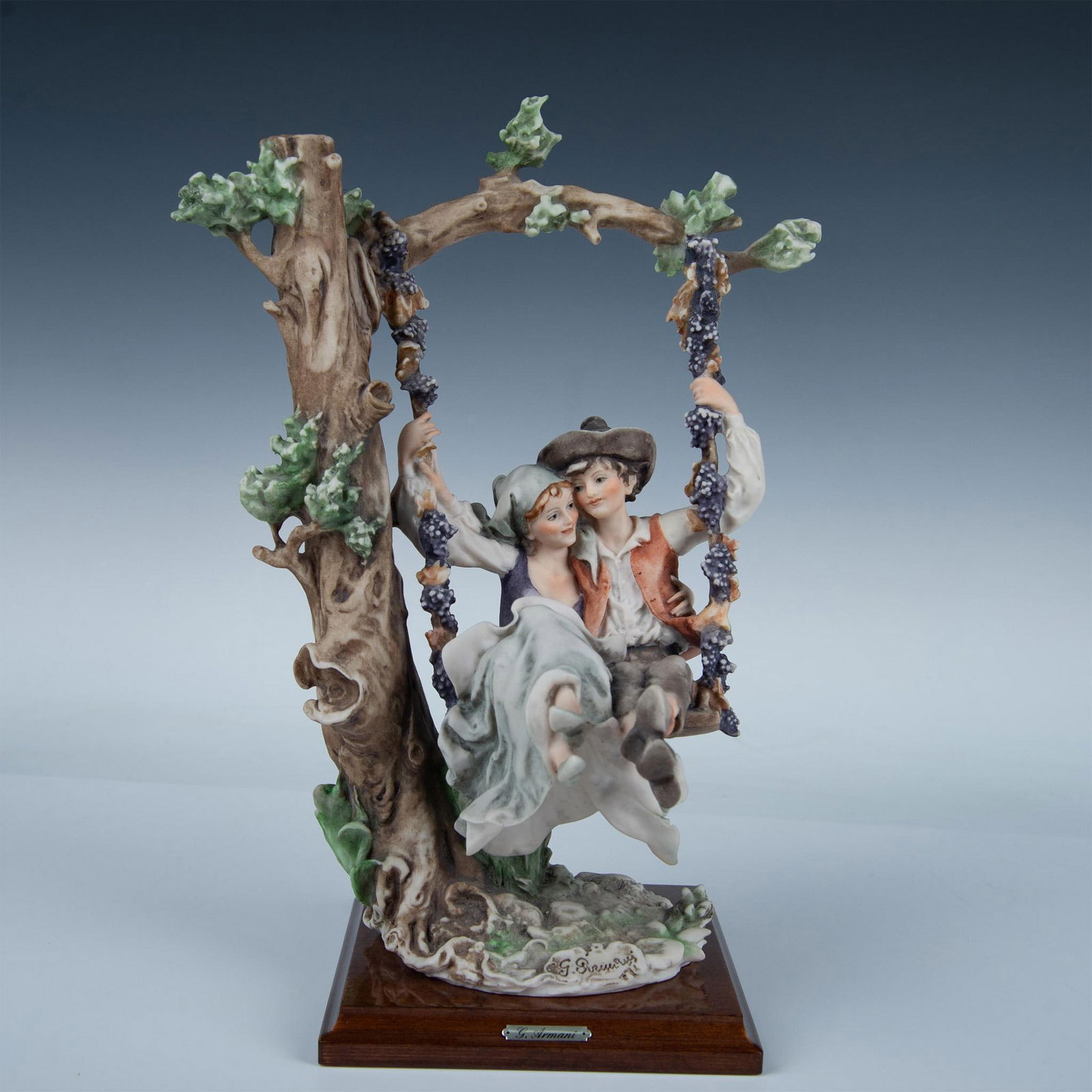 Capodimonte Giuseppe Armani Figurine, Autumn Swing: Hand modeled and hand painted figure of a boy and girl on a swing in a loving embrace. Vines of grapes coils around the ropes of the swing. Attach to a wooden base with Giuseppe Armani plaque. Marked