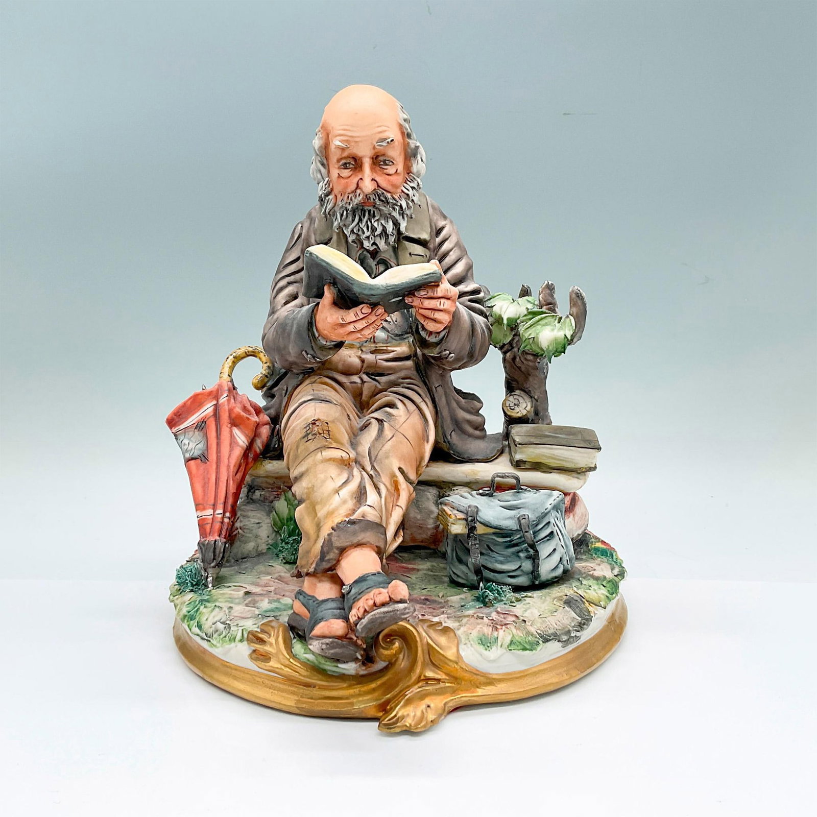 Capodimonte by Milio Porcelain Figurine, Tramp: Hand painted figure if a seated vagrant reading. Excellent details in the wrinkle of his clothes, and expression of his face. Marked on the underside: Capodimonte 108 Italy. Artist signed on the back.