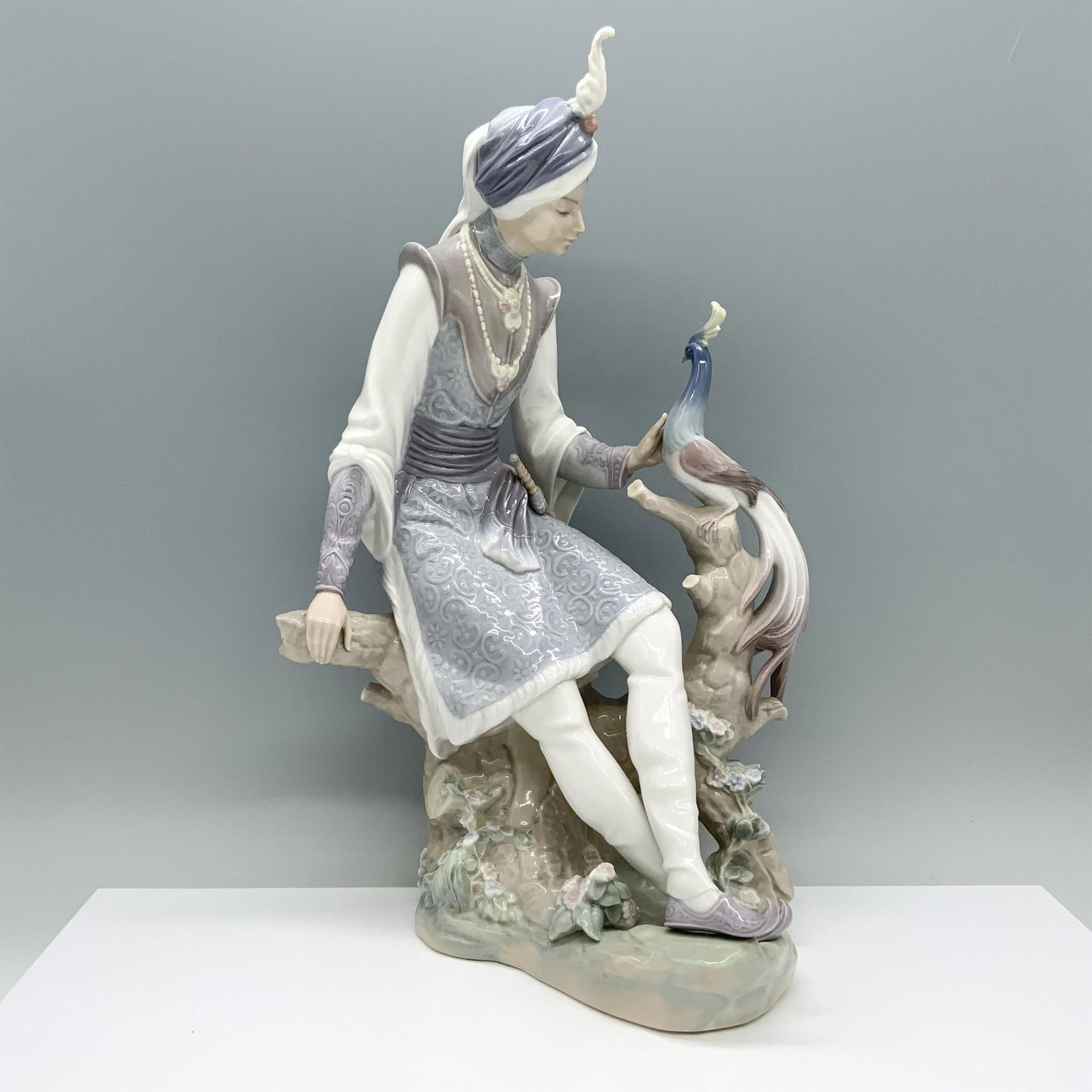 Arabian Knight 1001310 - Lladro Porcelain Figurine: A glazed figurine depicting a man in royal attire seated on a tree stump, gently caressing an exotic bird. Lladro backstamp. Artist: Salvador Debon Issued: 1974-1981 Dimensions: 8"L x 5.5"W x 14.75"H 