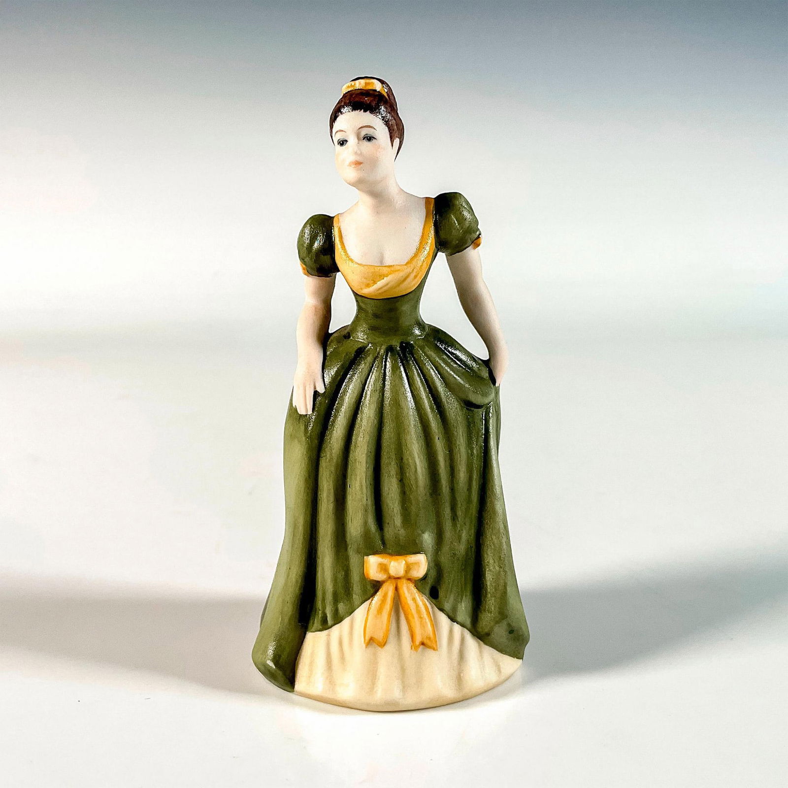 Goebel Porcelain Figurine, Justina: Hand painted in matte finish. She wears a charming green gown and is in bow position. Goebel backstamp. Issued: 20th c. Dimensions: 2.25"L x 2.25"W x 5"H Manufacturer: Goebel Country of Origin: German