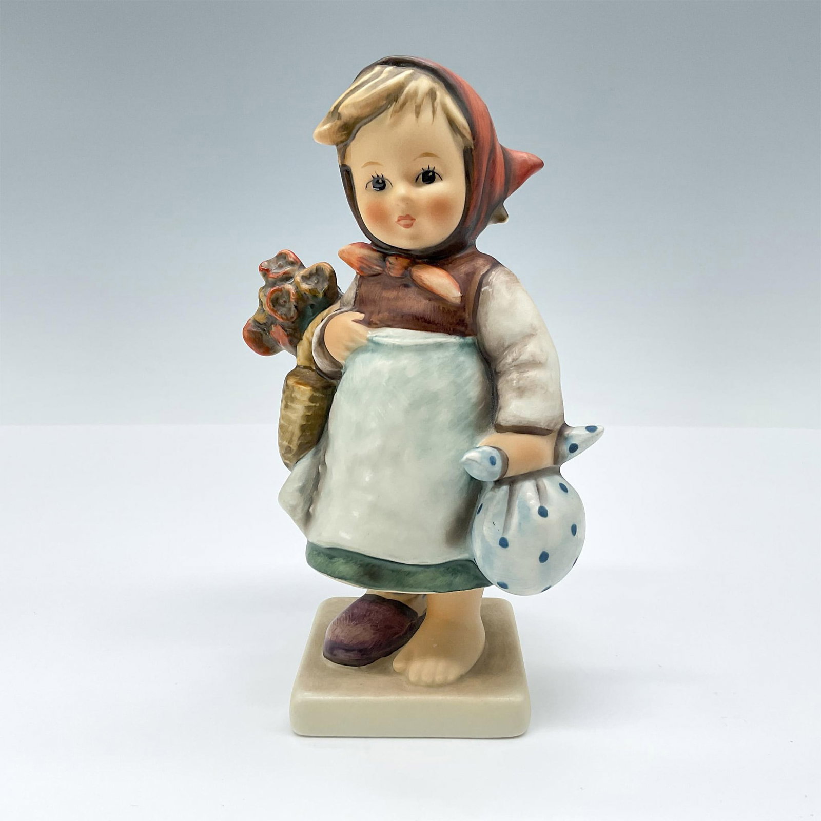 Goebel Hummel Figurine, Weary Wanderer HUM204: A rosy-cheeked weary girl holds a satchel and basket of flowers. One of her shoes has gone missing in her travels. TMK#6. Issued: 1979-1990 Dimensions: 3.5"L x 2.5"W x 5.75"H Manufacturer: Goebel Humm