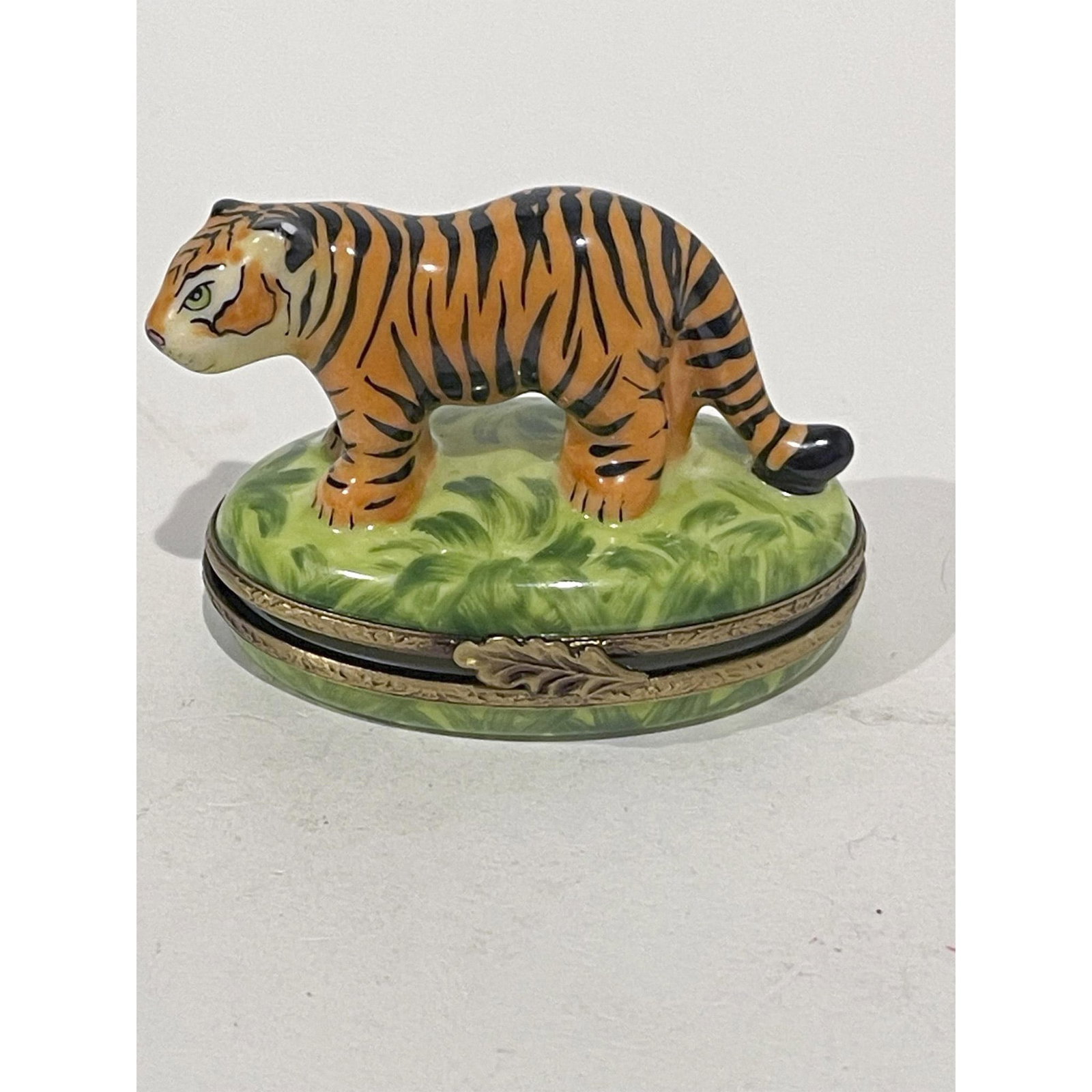Limoges France Keepsake Box, Striped Roaming Tiger: Limited Edition. Ferocious and majestic roaming tiger on grass is hand painted in vibrant colors atop this hinged oval porcelain mini box. A gilded leaf clasp opens box revealing the canine teeth in t
