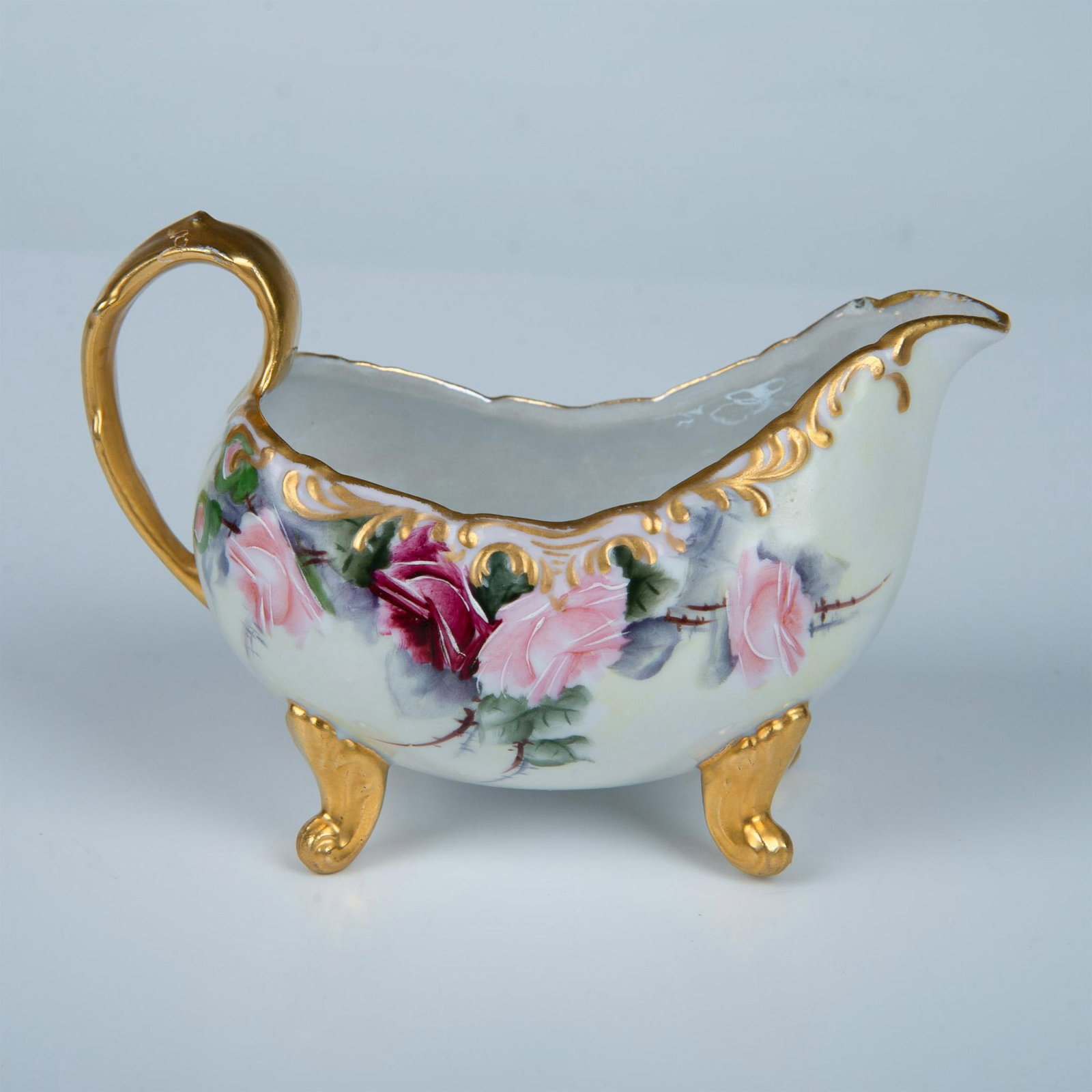 Nunda N.Y. by W.L. Dailey Porcelain Gravy Boat: A hand painted quad-footed tableware. Decorated with pink and purple roses and gilt on the handle and feet. Nunda N.Y. and W.L. Dailey marked on the underside. Artist: W.L. Dailey Issued: Early 20th c