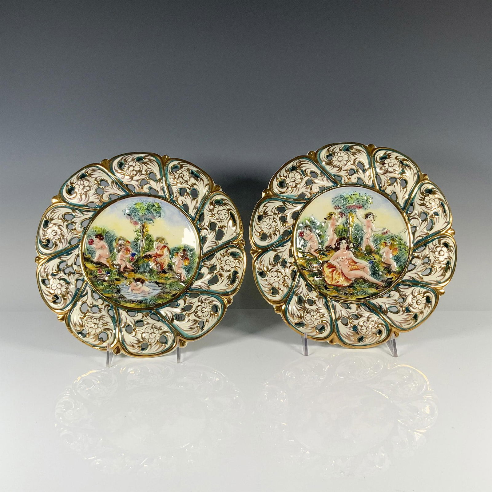 2pc L.B.S Italian Capodimonte Style Decorative Wall Plates: Exquisite plates featuring delicate flower petal designs encircling captivating scenes, one, a playful depiction of children by a puddle, the other, a serene portrayal of nude women amidst nature. Mar