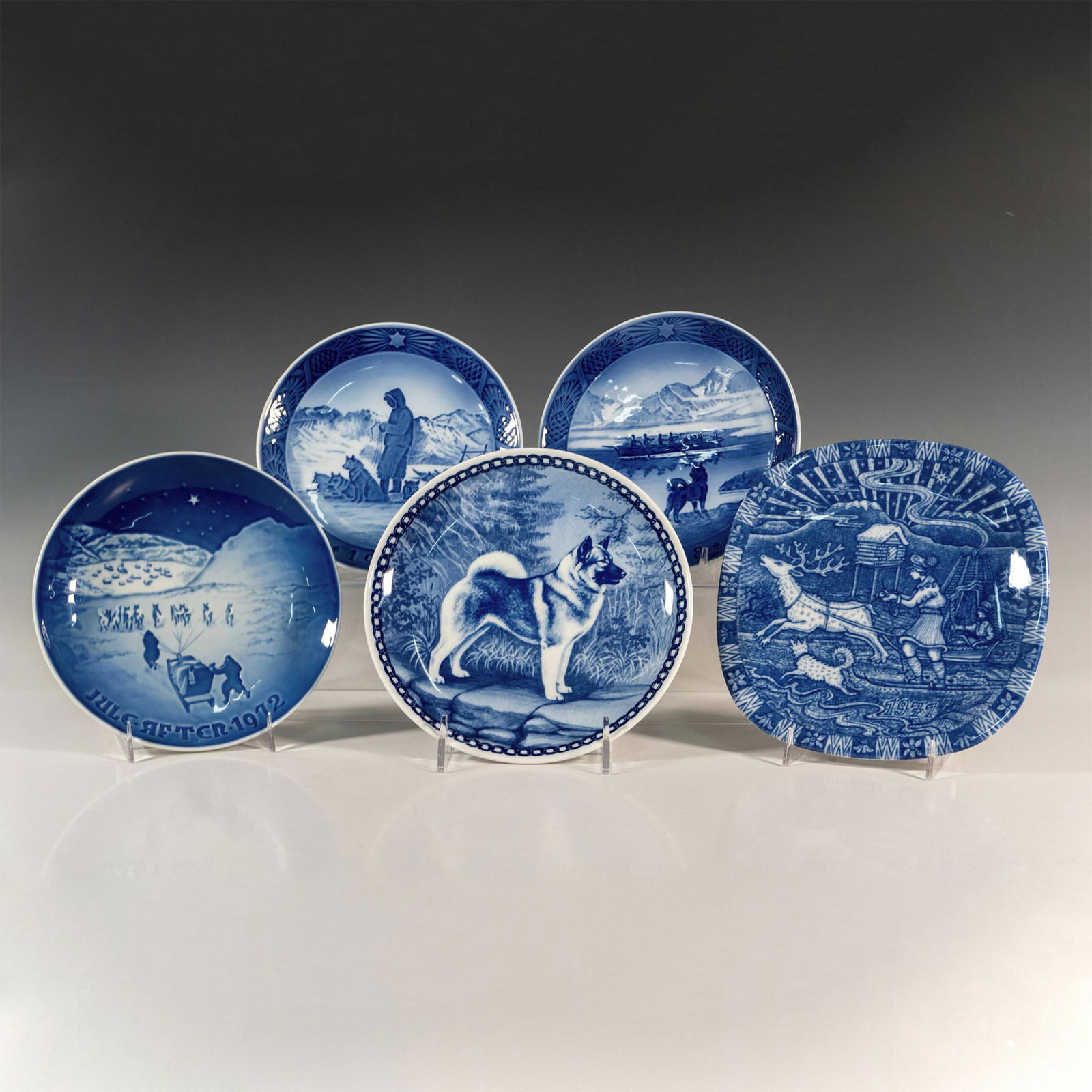 5pc Scandinavian Porcelain Blue and White Plaques: A collection of wall plates featuring Norwegian Elkhounds and their human companions. Includes 2 Royal Copenhagen, 1 Bing & Grondahl, 1 Julen Rorstrand, and 1 plate from Denmark. The largest plate mea