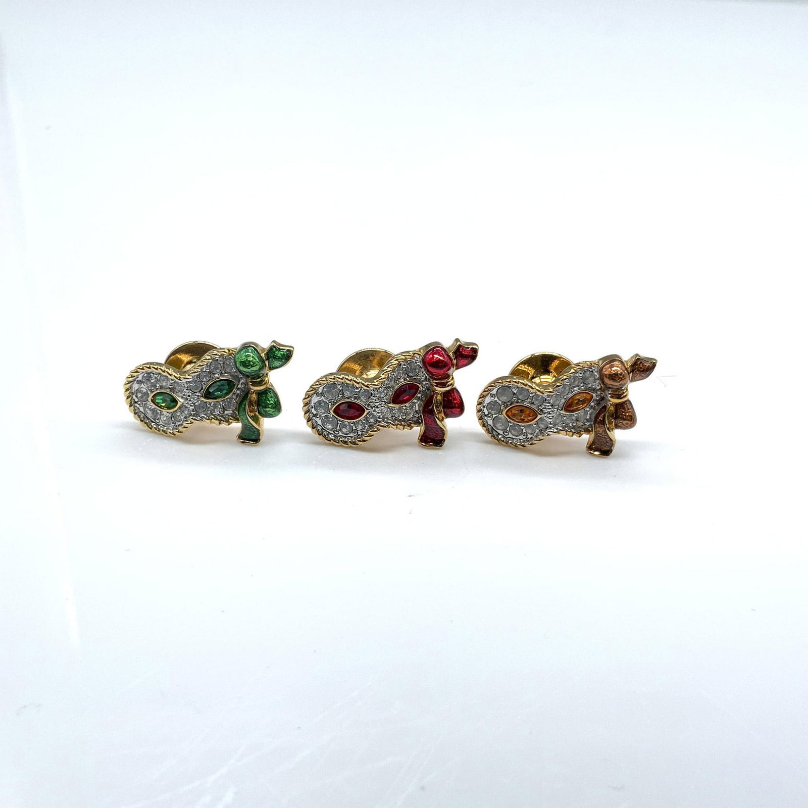 3pc Swarovski Red, Orange, and Green Mask Pins: The metal is gold, and the pins have clear and colored crystals. Dimensions: 0.75"L x 0.5"W Manufacturer: Swarovski