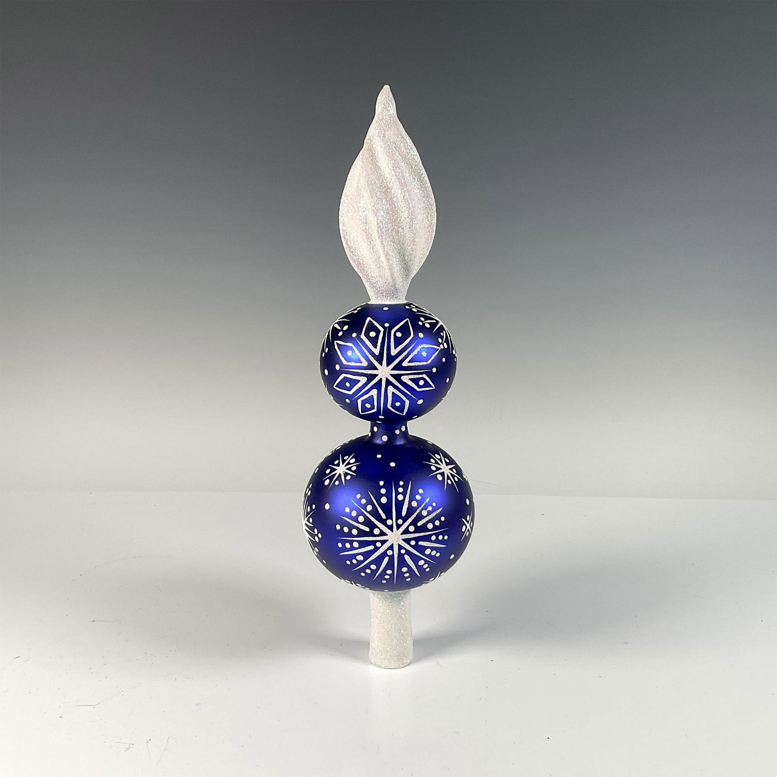 Patricia Breen Glass Blown Blizzard Finial/Tree Topper: This exquisite, handcrafted tree topper is adorned in royal blue with glittery snowflakes and accents in the Blizzard pattern, adding a touch of elegance to any Christmas tree. Dimensions: 13"H x 4" d