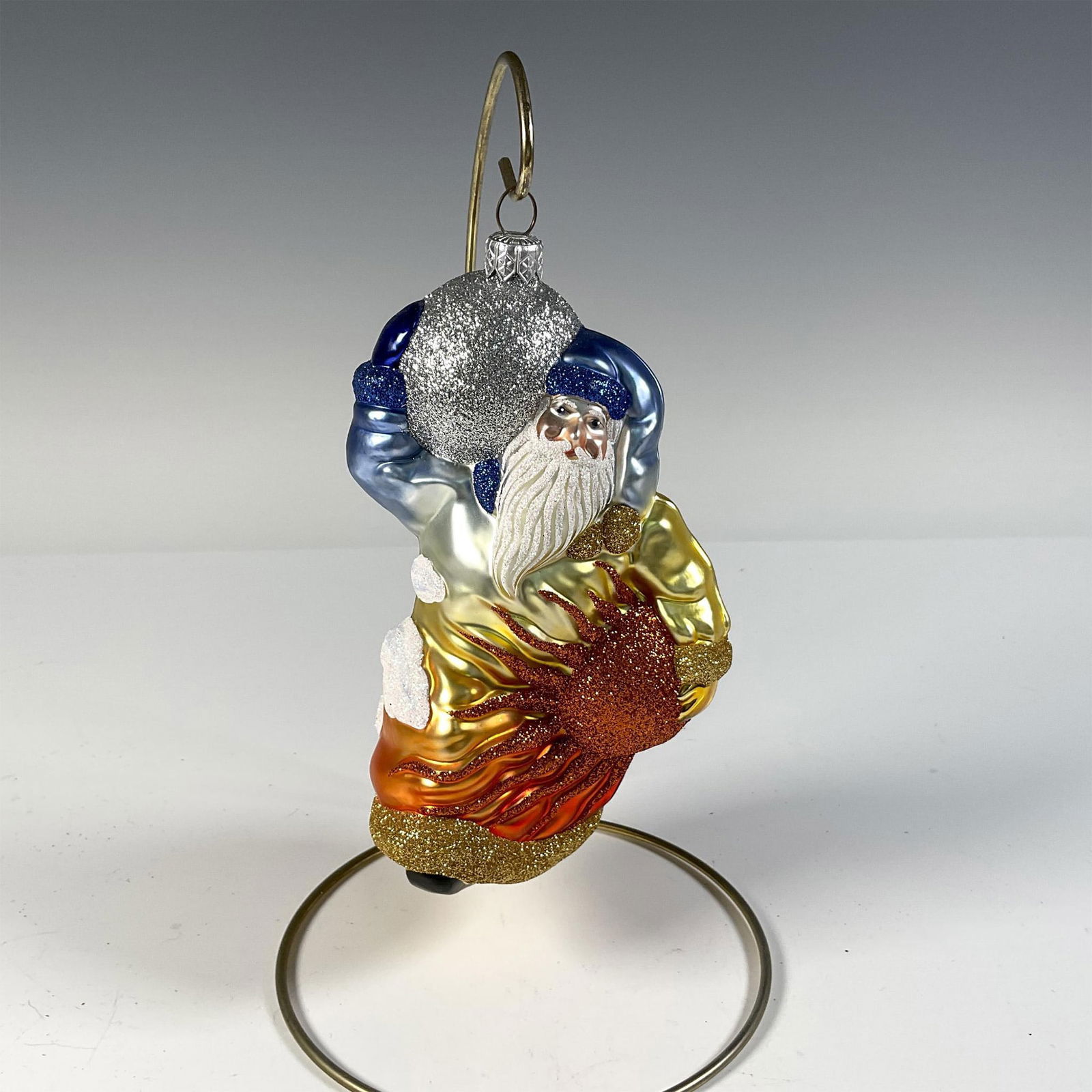 Patricia Breen Ornament Planetary Santa, Blue and Orange: Stunning hand-painted European-style glass Christmas ornament depicting Santa with the sun and moon, all embellished with sparkling glitter. Issued: c. 2000 Dimensions: 4"L x 3.5"W x 7"H Manufacturer: