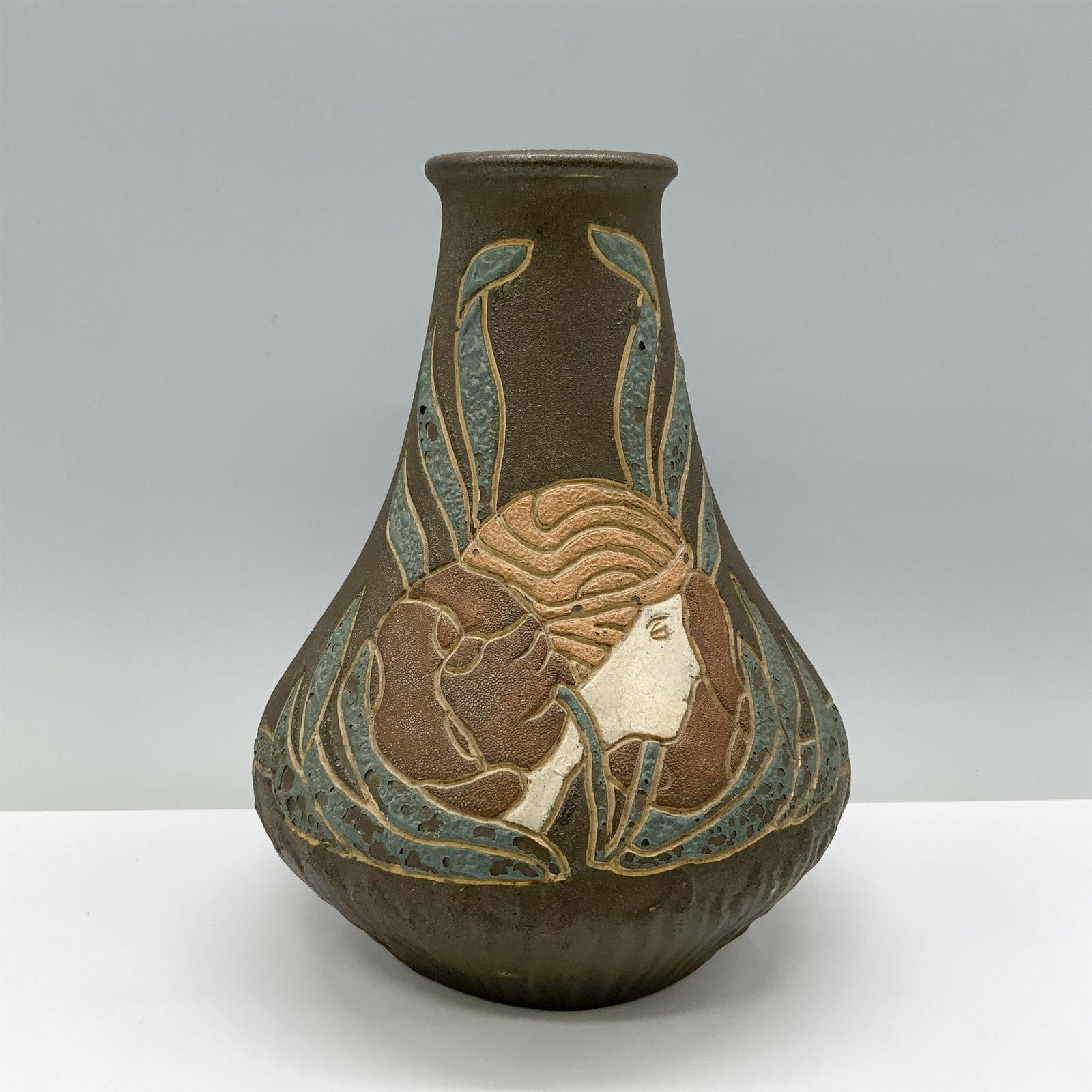 Owens Henri Deux Art Pottery Vase: A rustic brown vase embellished with aqua accents, showcasing a woman's face on one side and abstract art on the other. Marked Henri Deux 1306. Dimensions: 8.25"H x 6.25" dia. Manufacturer: Owens Coun
