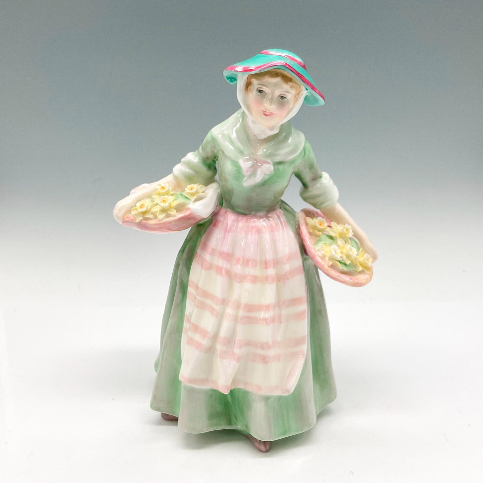 Daffy Down Dilly - HN1712 - Royal Doulton Figurine: Part of the Harradine Classics series. Colored in mint green with pink and cream apron carrying baskets of flowers. Royal Doulton backstamp. Artist: Leslie Harradine Issued: 1935 - 1975 Dimensions: 4.