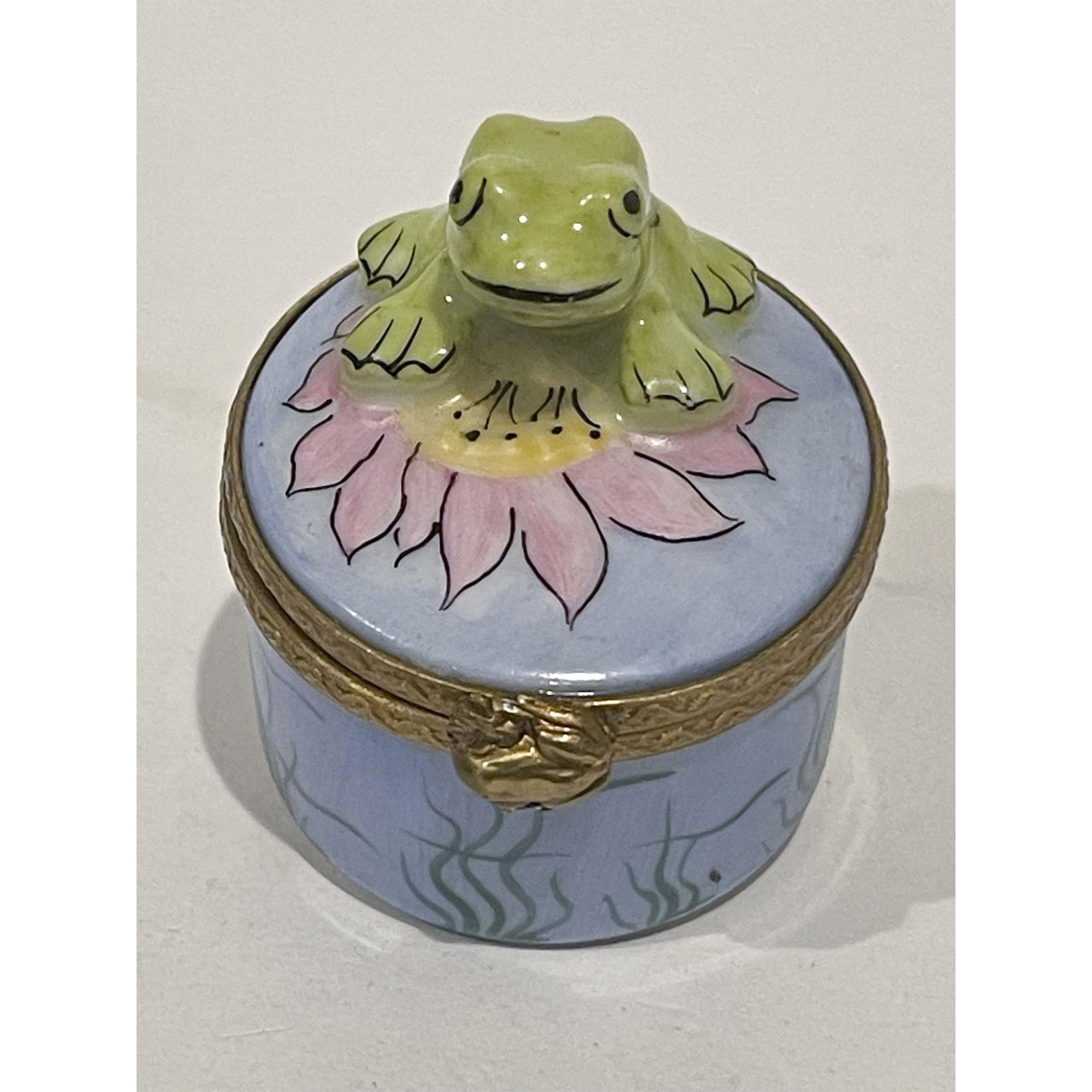 Limoges France Keepsake Box, Frog on Flower Artist Initials: Precious Green Frog on Pink Lily Pad flower atop hand painted blue porcelain mini box decorated and beautifully detailed with deeper green water grass all around. Gilded frog clasp opens to reveal gre