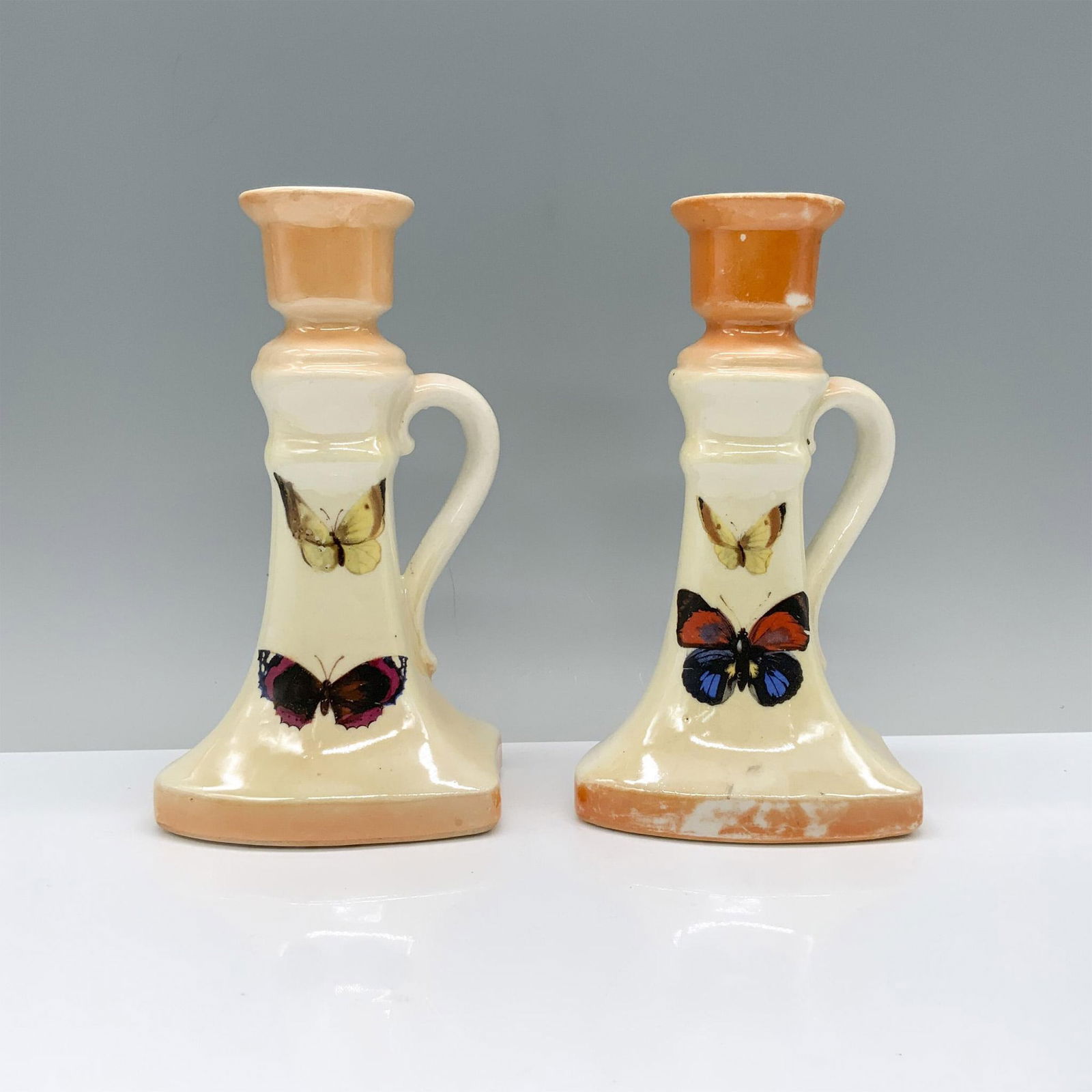 2pc Czechoslovakian Butterfly Candlesticks: Yellow and orange candlesticks with butterfly artwork at the center, featuring handles for easy transportation. Marked Czecho-Slovakia. Dimensions of the largest item: 3.5"L x 3.5"W x 6.25"H. Country