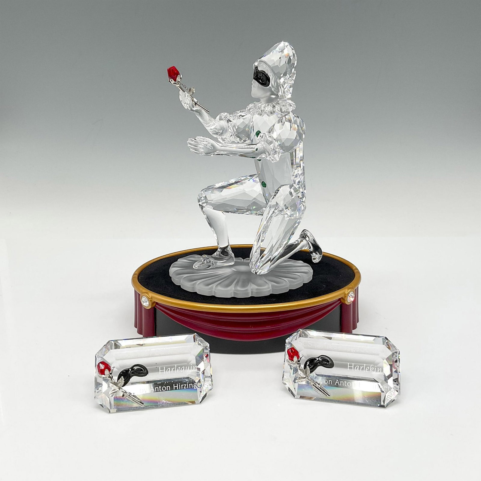 Swarovski SCS Figurine, Masquerade Harlequin + Base, Plaques: Harlequin is the final piece of the Masquerade trilogy. Created in clear, frosted and black crystal, and holds a red crystal rose. Two Harlequin plaques included in English and German. Swarovski backs