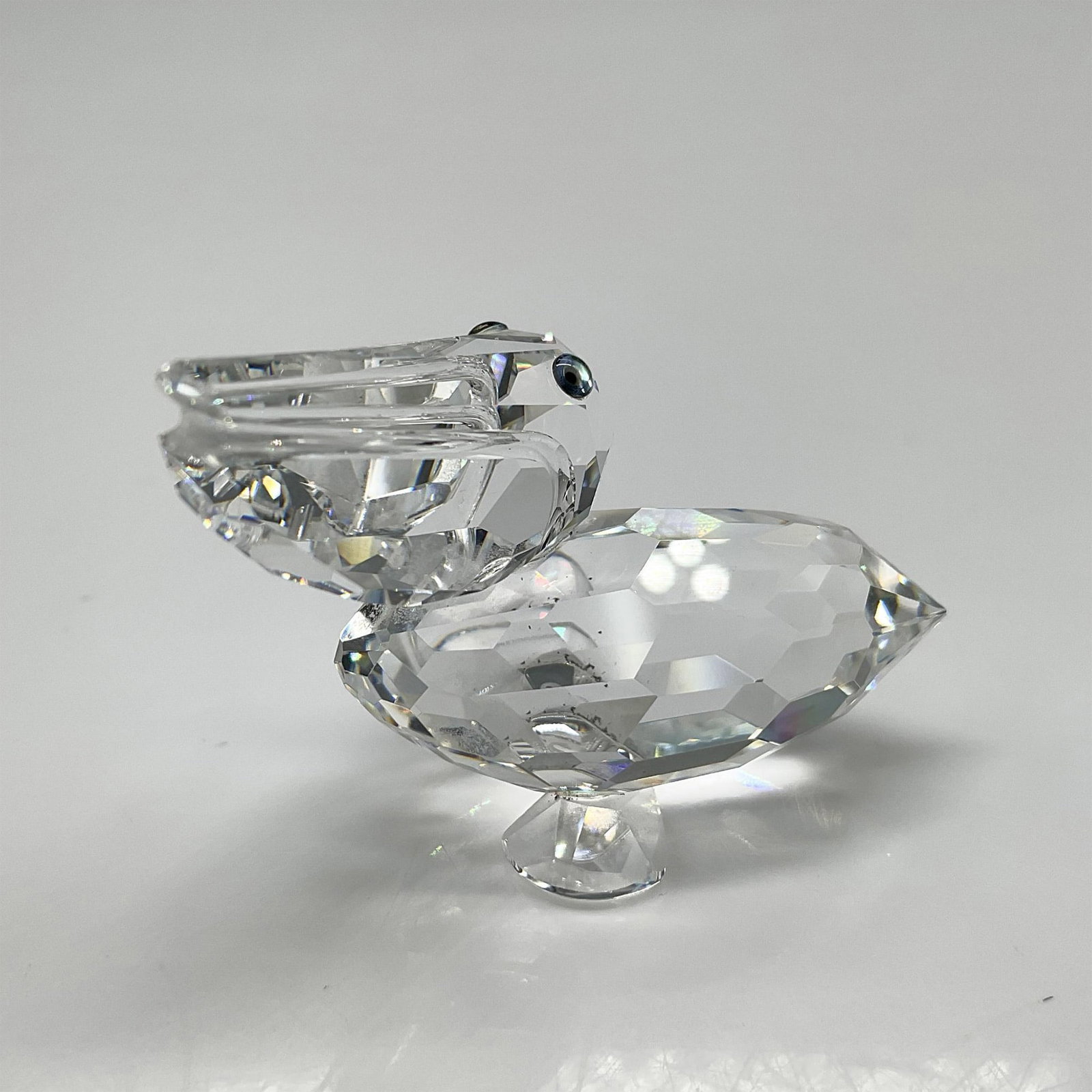 Swarovski Silver Crystal Figurine, Pelican: Part of the Feathered Friends collection is created from clear crystal with blue crystal eyes. Swarovski backstamp. 7679 000 001. This item has its original box 2.5"H x 3.25" dia. Artist: Anton Hirzin