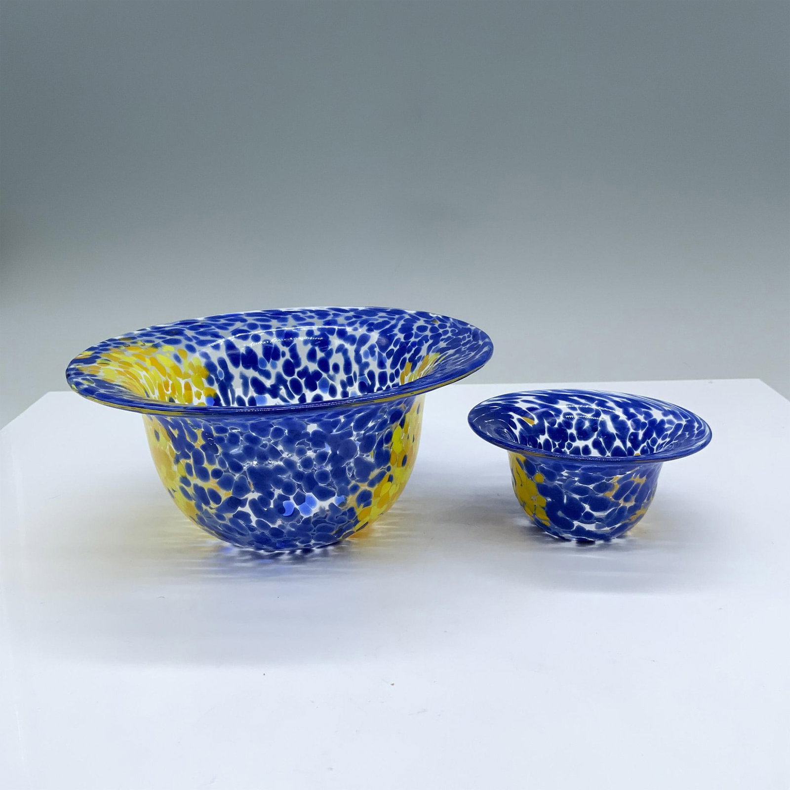 2pc Kosta Boda Art Glass Bowls by Ulrica Hydman: Two blue and yellow art glass bowls with artist signatures on the bottoms. The larger bowl measures approximately 6.5"dia. x 3"H. The smaller bowl measures approximately 3.75"dia. x 1.75"H. Artist: Ul