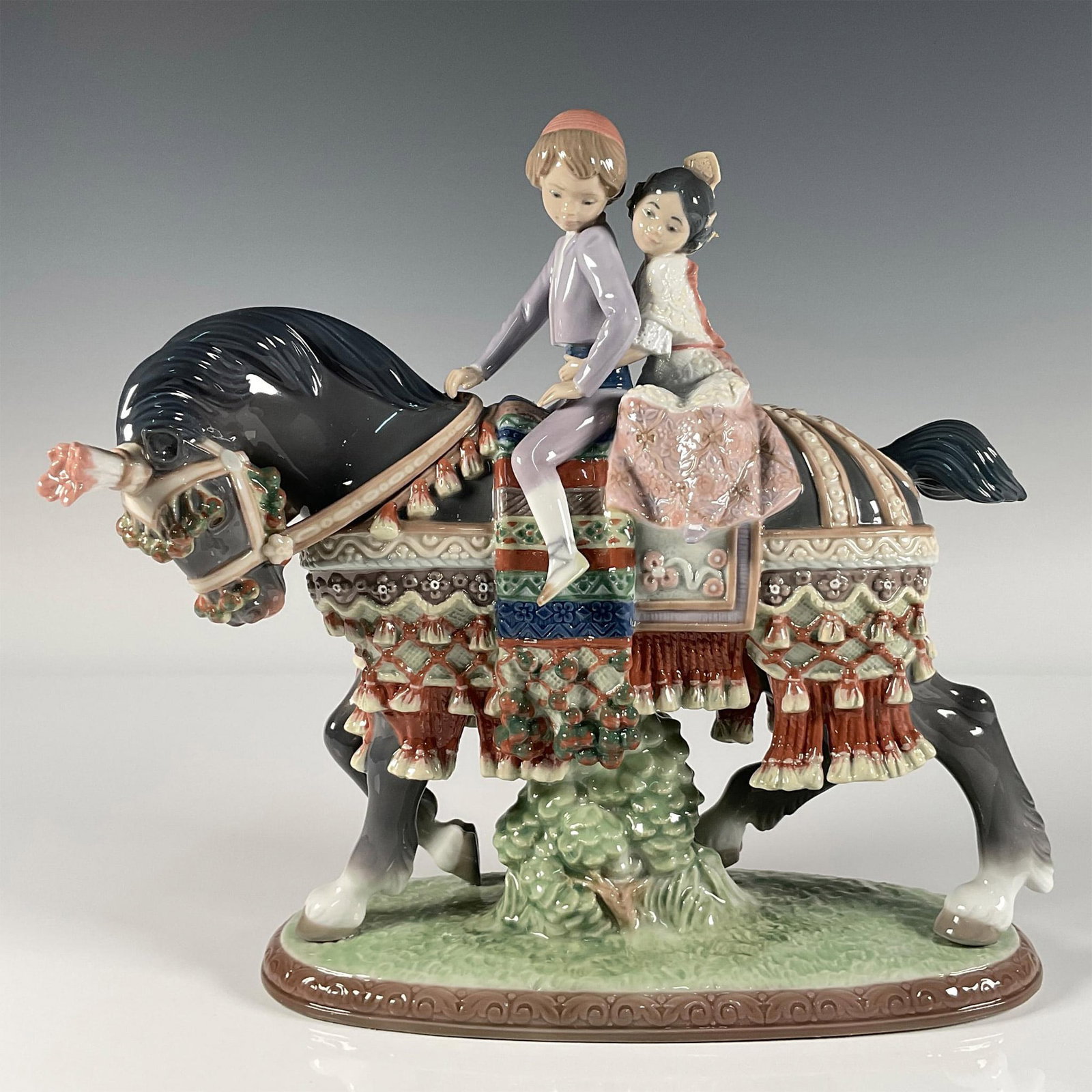 Valencian Children 1001489 - Lladro Porcelain Figurine: Glossy finish; two children in traditional clothing, riding an elegantly saddled horse. Lladro backstamp. This item has its original box. Box measures: 12.755"L x 15.25"W x 9"H. Artist: Francisco Cata