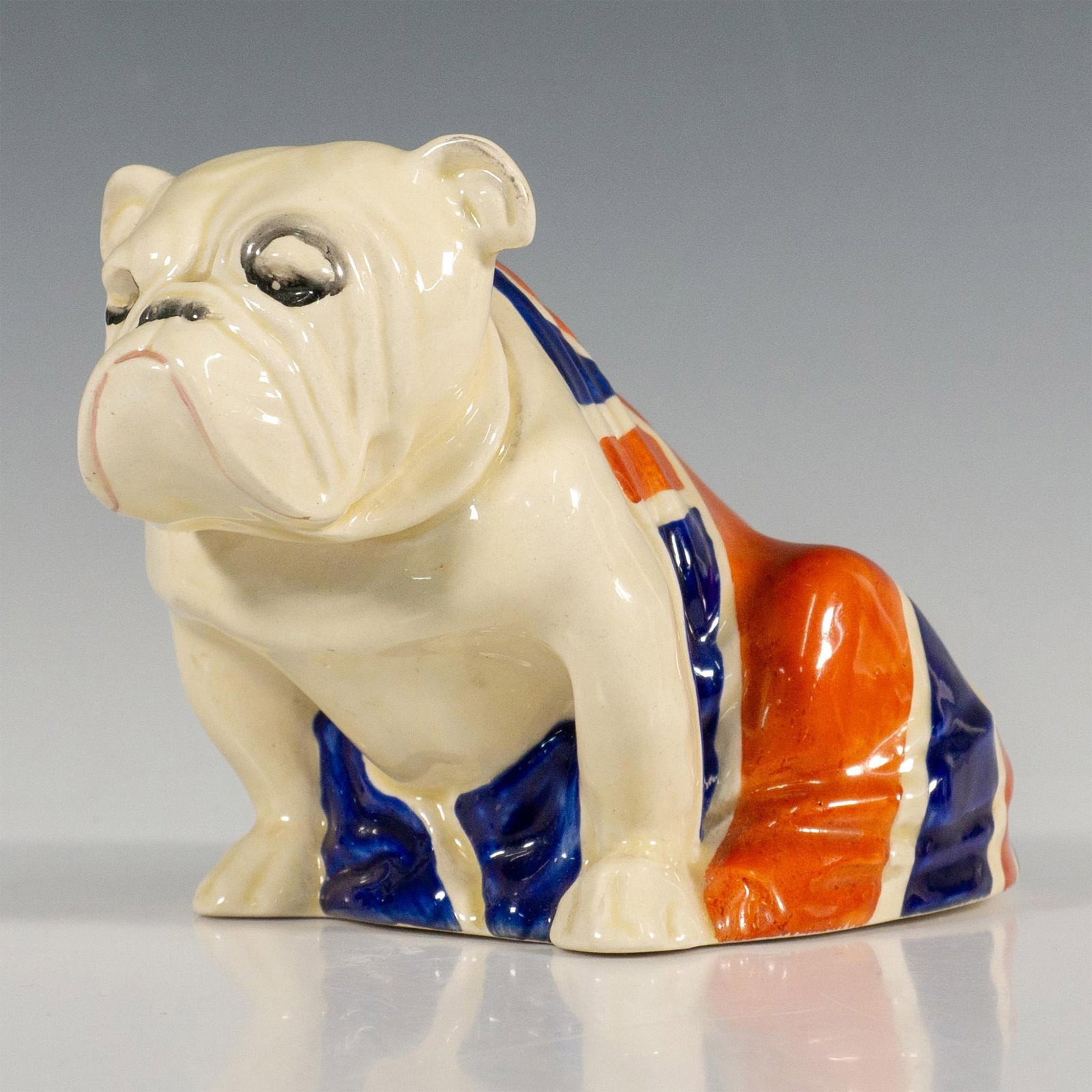 Union Jack Bulldog - D5913 - Royal Doulton Figurine: Hand painted medium size seated Bulldog figurine with black collar draped in the Union Jack. Royal Doulton backstamp in black. Issued: 20th century Dimensions: 6"L x 3.25"W x 3.75"H Manufacturer: Roya