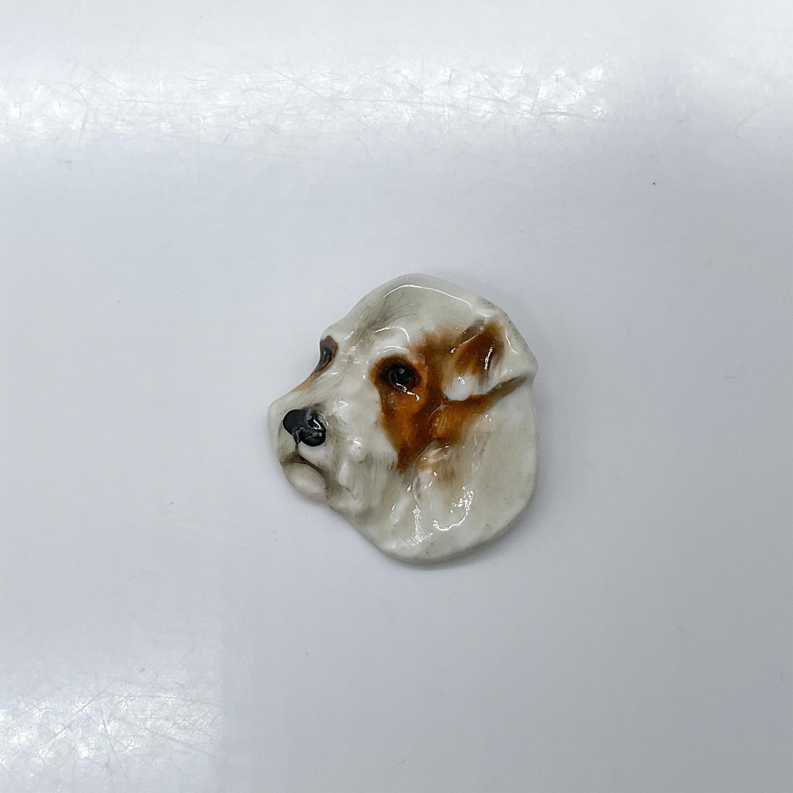 Royal Doulton Dogs Head Brooch, Sealyham: Pottery pin molded as a terrier head; needle pin fasten. White and brown coloration. Royal Doulton impressed stamp. Issued: 1930s Dimensions: 1.5"W x 1.5"H x 0.5"D Manufacturer: Royal Doulton Country 