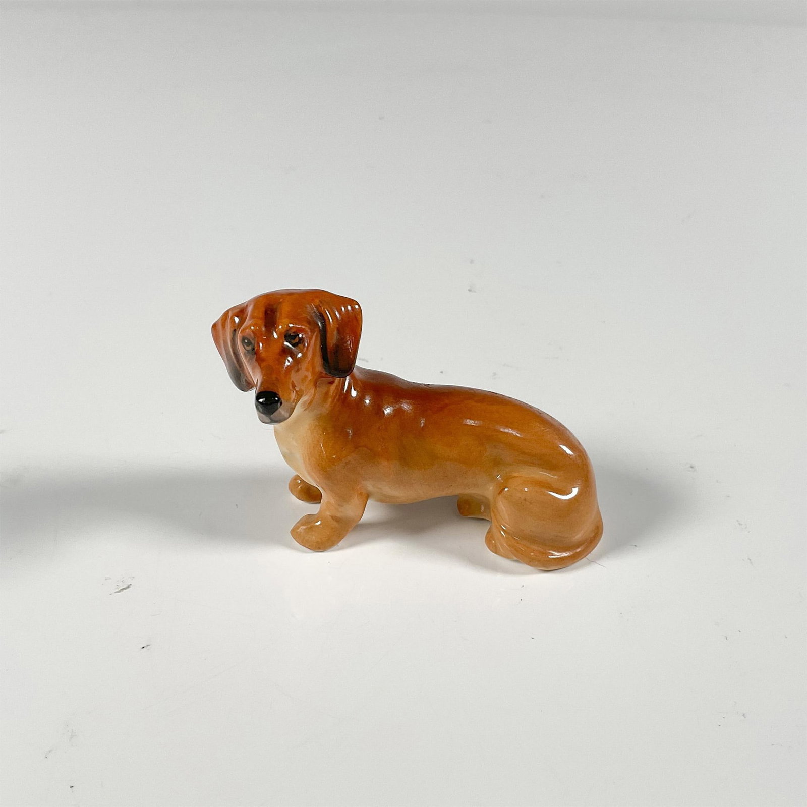 Royal Doulton Porcelain Dog Figurine, Mini Dachshund K17: Miniature Dachshund K17. Gloss finish. Royal Doulton backstamp in green. Issued: 20th century Dimensions: 2.5"L x 1.25"W x 1.75"H Manufacturer: Royal Doulton Country of Origin: England