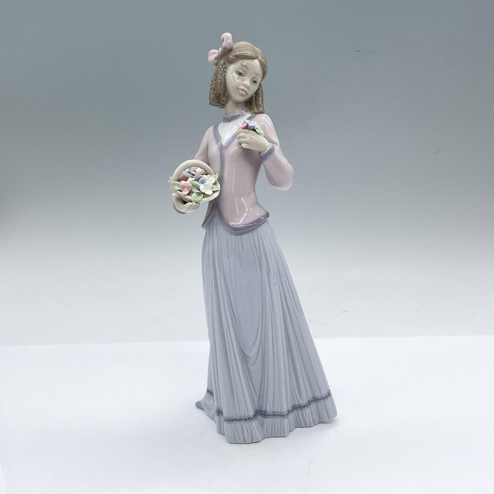 Innocence In Bloom 1007644 - Lladro Porcelain Figurine: Glossy finish; Lladro backstamp. Includes original box: 12"L x 6.75"W x 5.5"H. Artist: Jose Puche Issued: 1996 - 1996 Dimensions: 4"L x 3.75"W x 9.75"H Manufacturer: Lladro Country of Origin: Spa