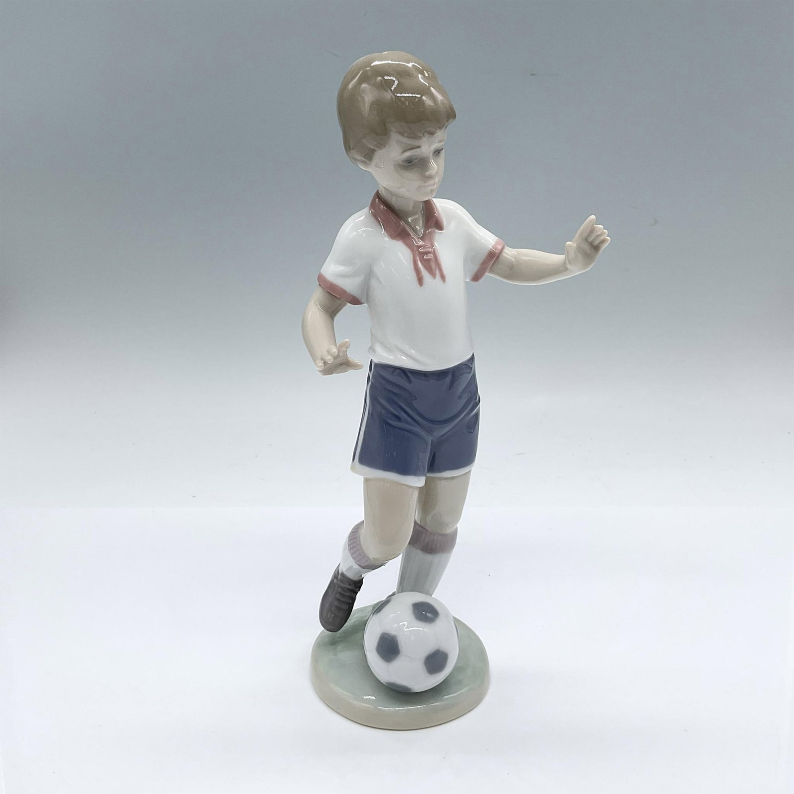 Soccer Practice 1006198 - Lladro Porcelain Figurine: Glossy finish; Lladro backstamp. Includes original box: 11"L x 5.75"W x 5"H. Artist: Miguel Angel Santaeulalia Issued: 1995 - 2010 Dimensions: 4"L x 3.25"W x 8.5"H Manufacturer: Lladro Country of Ori